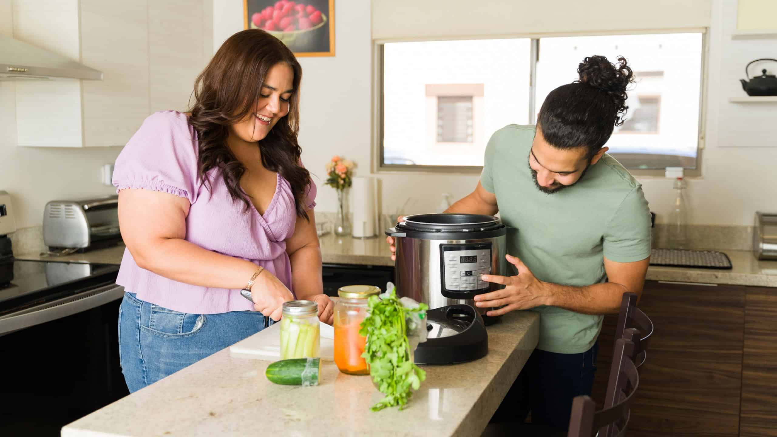 Happy beautiful couple laughing and having fun while preparing lunch or dinner in the pressure cooker doing house chores in the kitchen