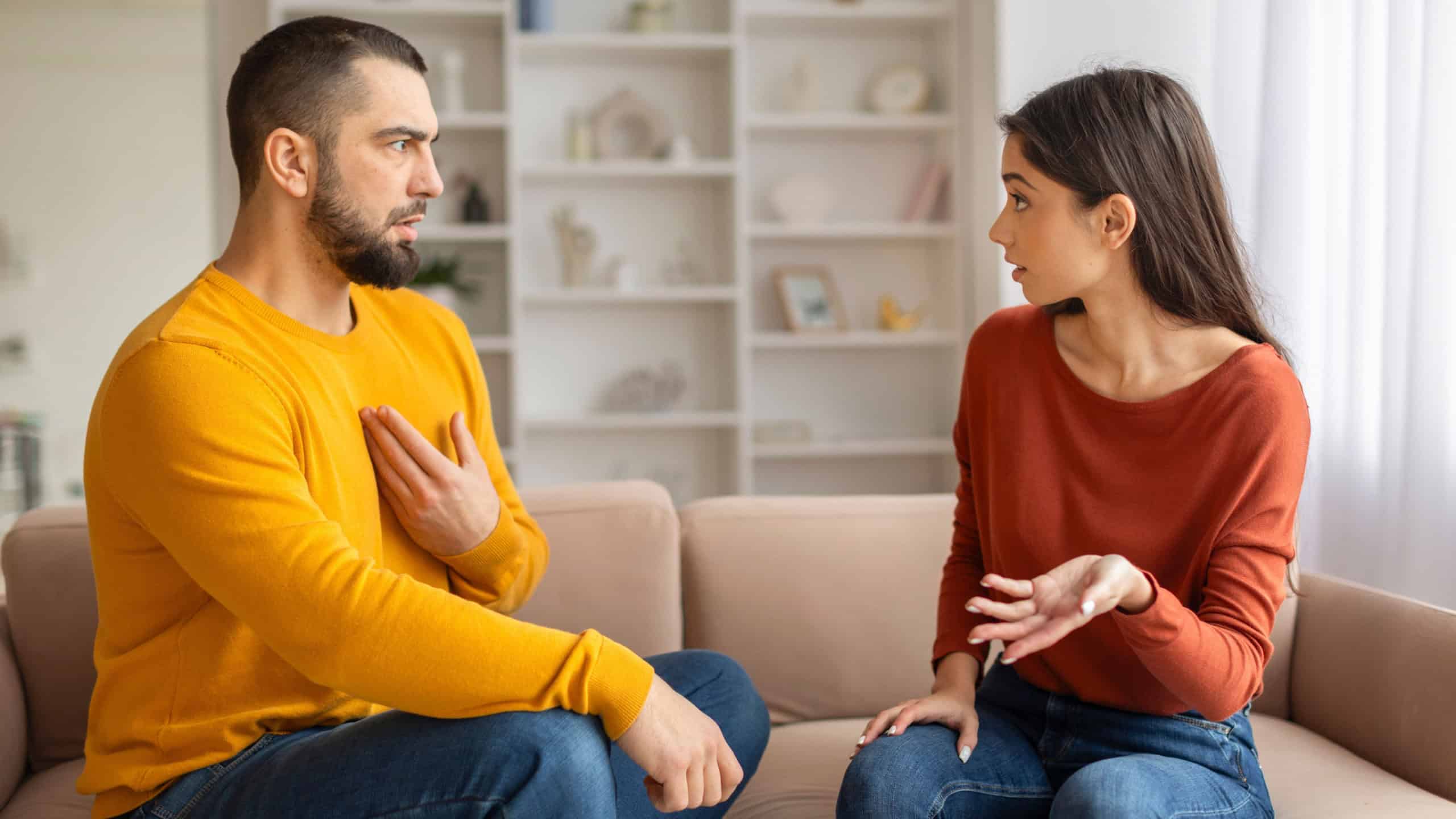 Young Couple Having Emotional Conversation While Sitting On Couch At Home, Millennial Spouses Arguing, Suffering Relationship Crisis And Misunderstanding, Quarrelling With Each Other