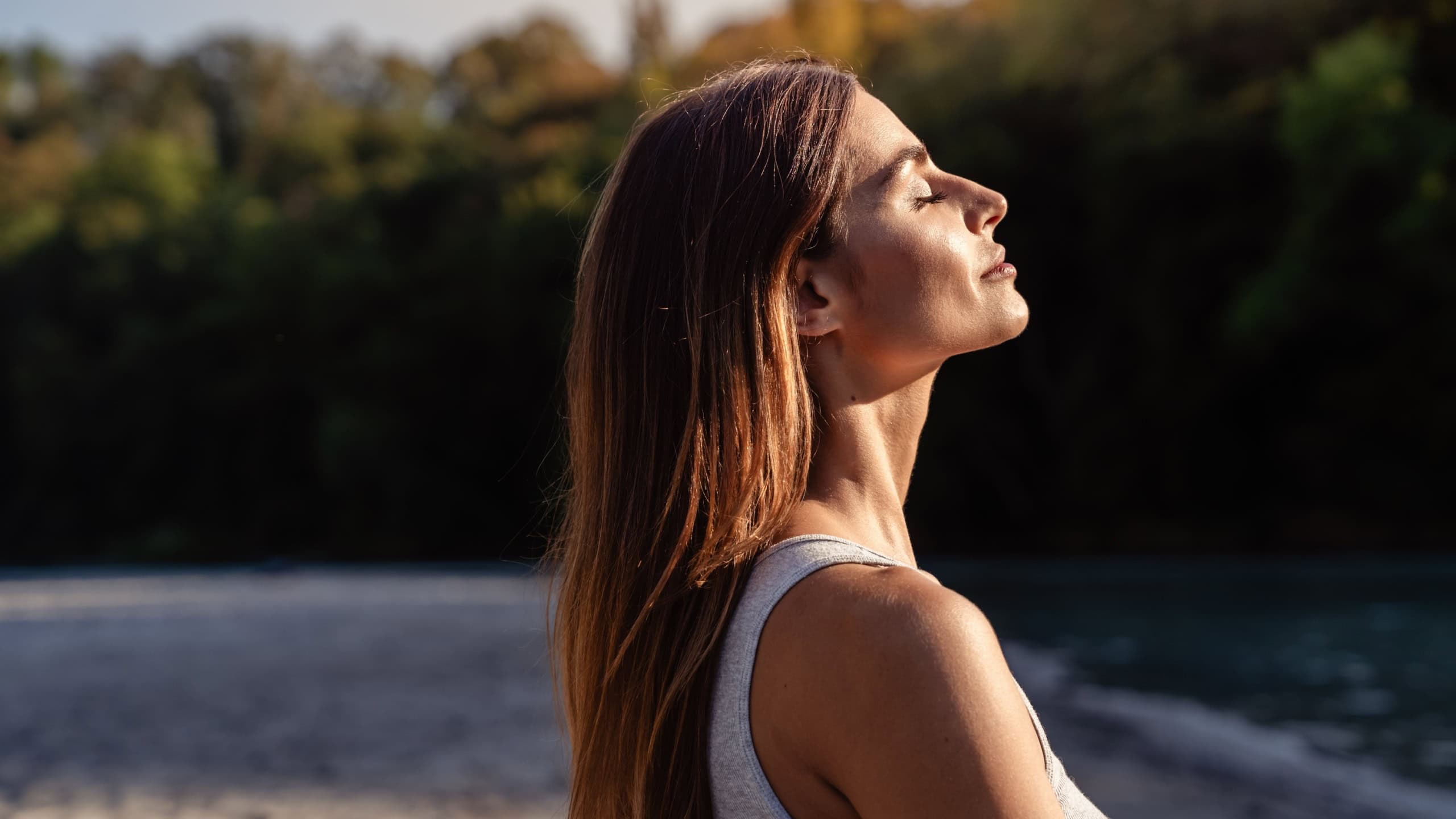 Young woman with long hair enjoying sun with closed eyes getting natural vitamin D outdoors. Peace of mind. Mindfulness, mental health, spirituality, well-being, unwind yourself