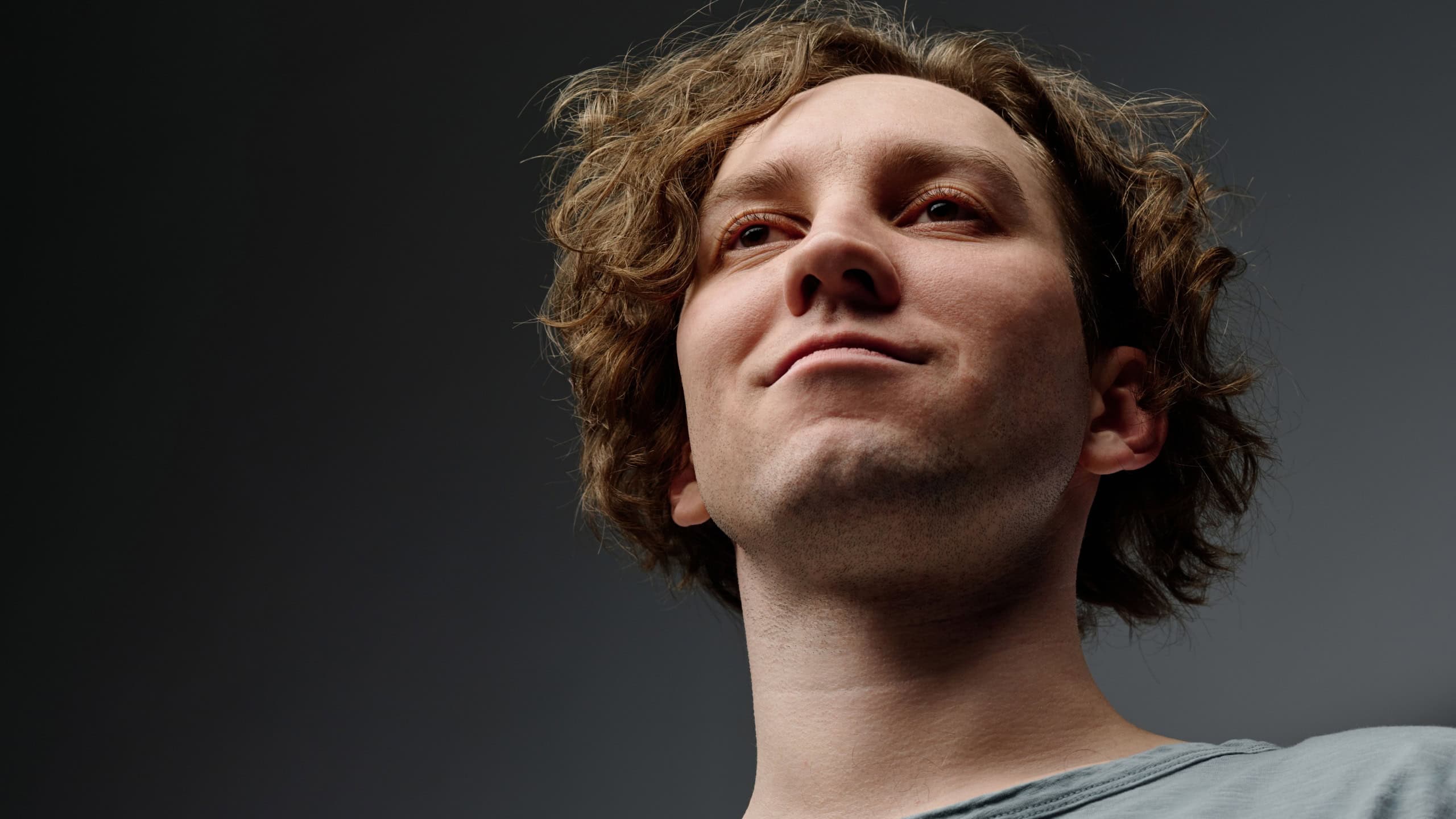 Low angle closeup studio portrait of self-confident young Caucasian man with curly hair smirking, copy space
