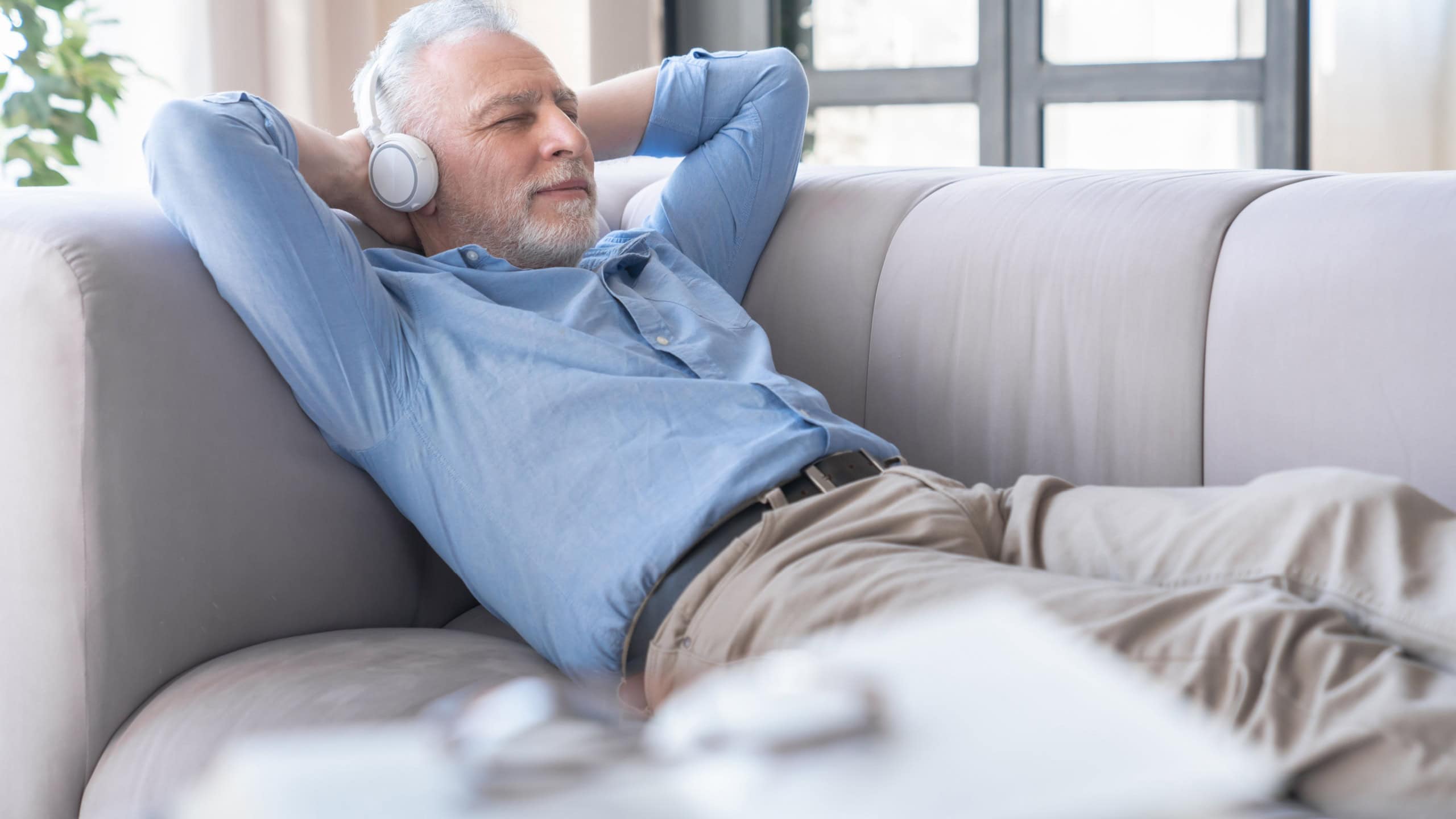 Relaxed old elderly senior mature man grandfather listening to the music podcast e-book in headphones earphones, having rest chilling on the sofa at home. Active seniors concept