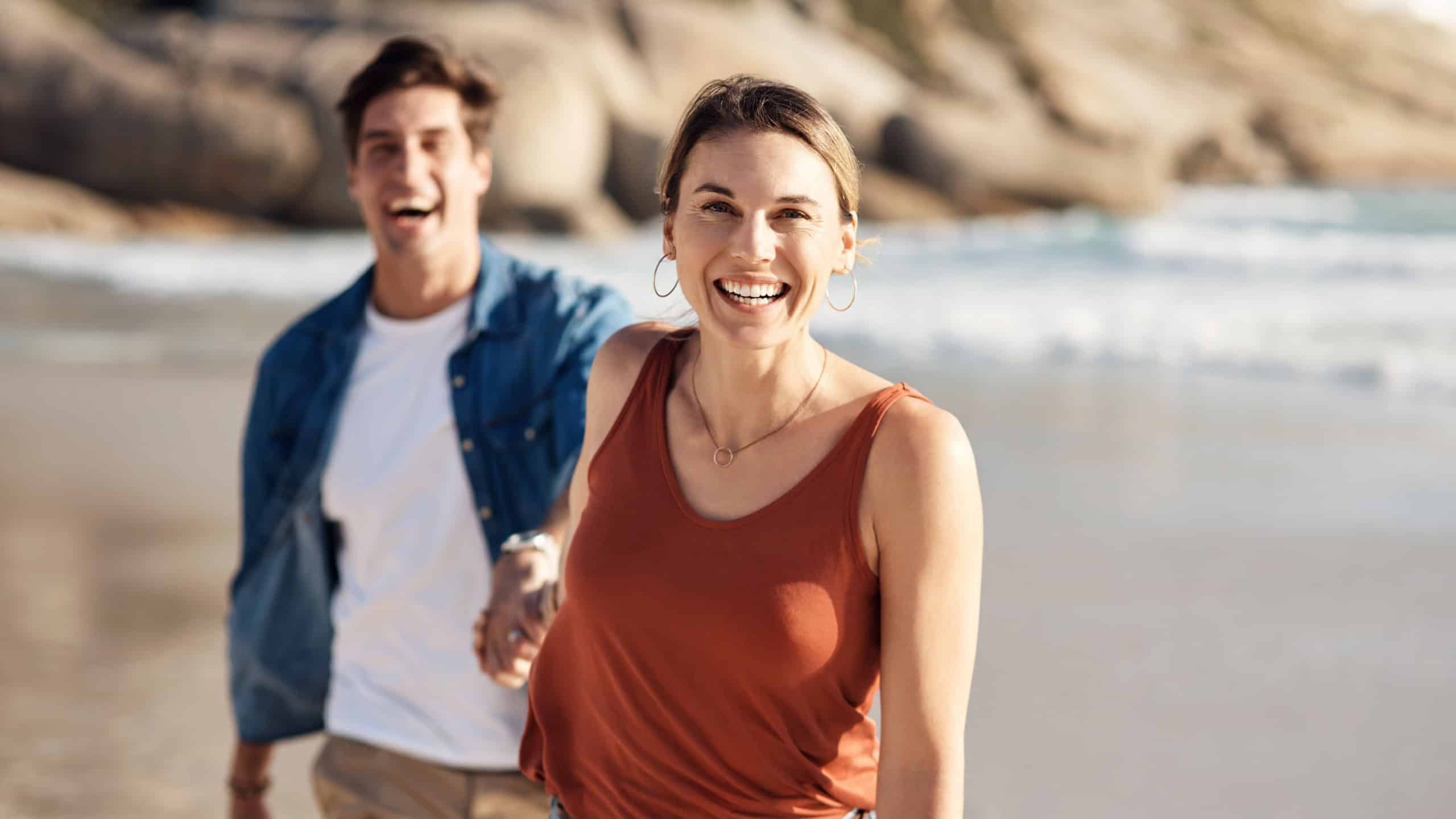 Couple, portrait and holding hands with woman at beach on journey in summer, holiday or vacation. Happy, travel and lead man with smile on face on island at sunset offshore and adventure in marriage