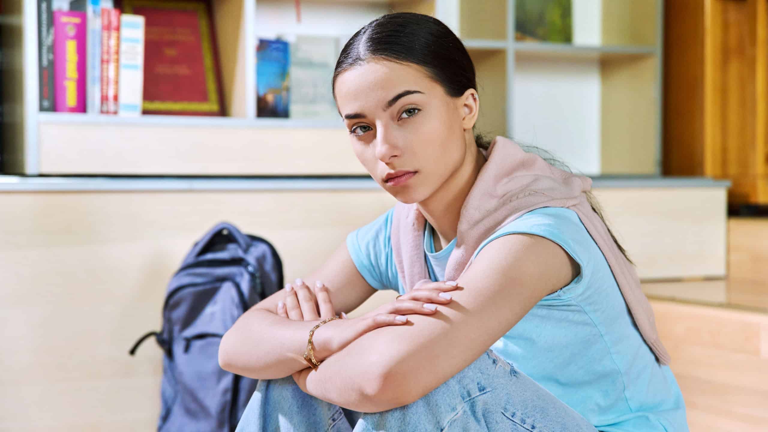 Serious teenage girl high school student sitting in class looking at camera