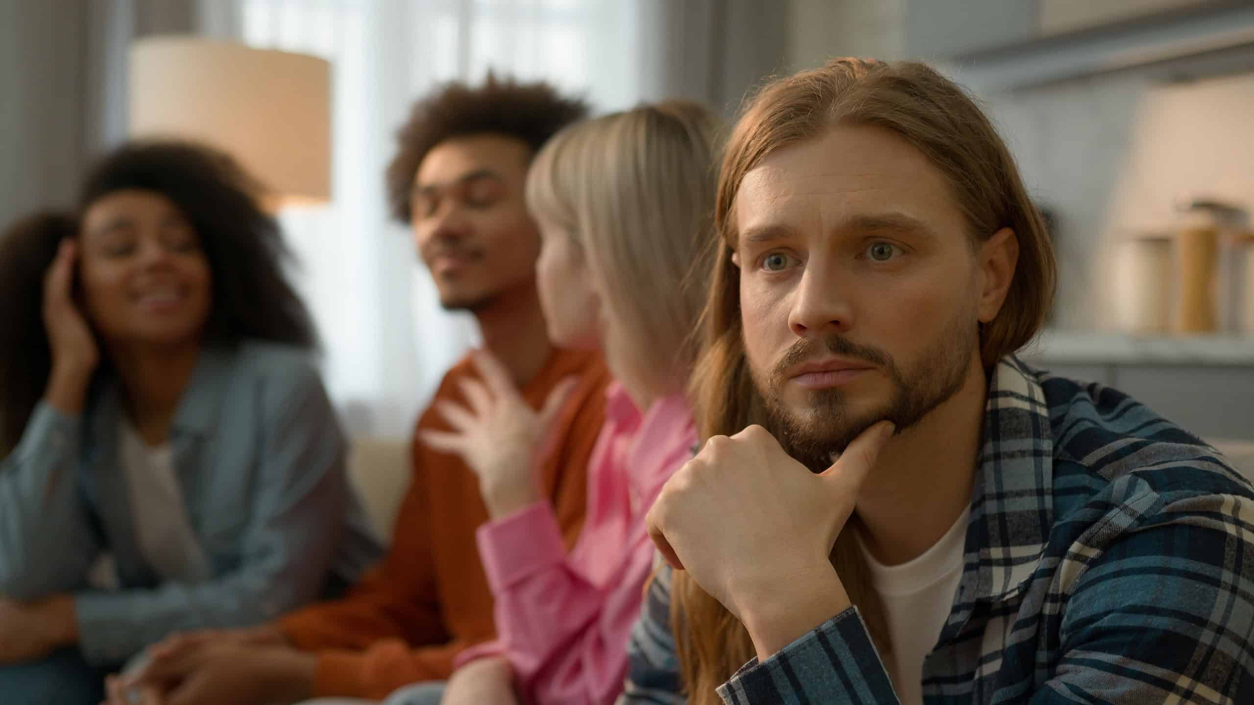 Caucasian sad pensive thinking troubled problem frustrated man guy introvert at home separated ignoring multiracial African multiethnic friends women men laughing talking antisocial outsider male