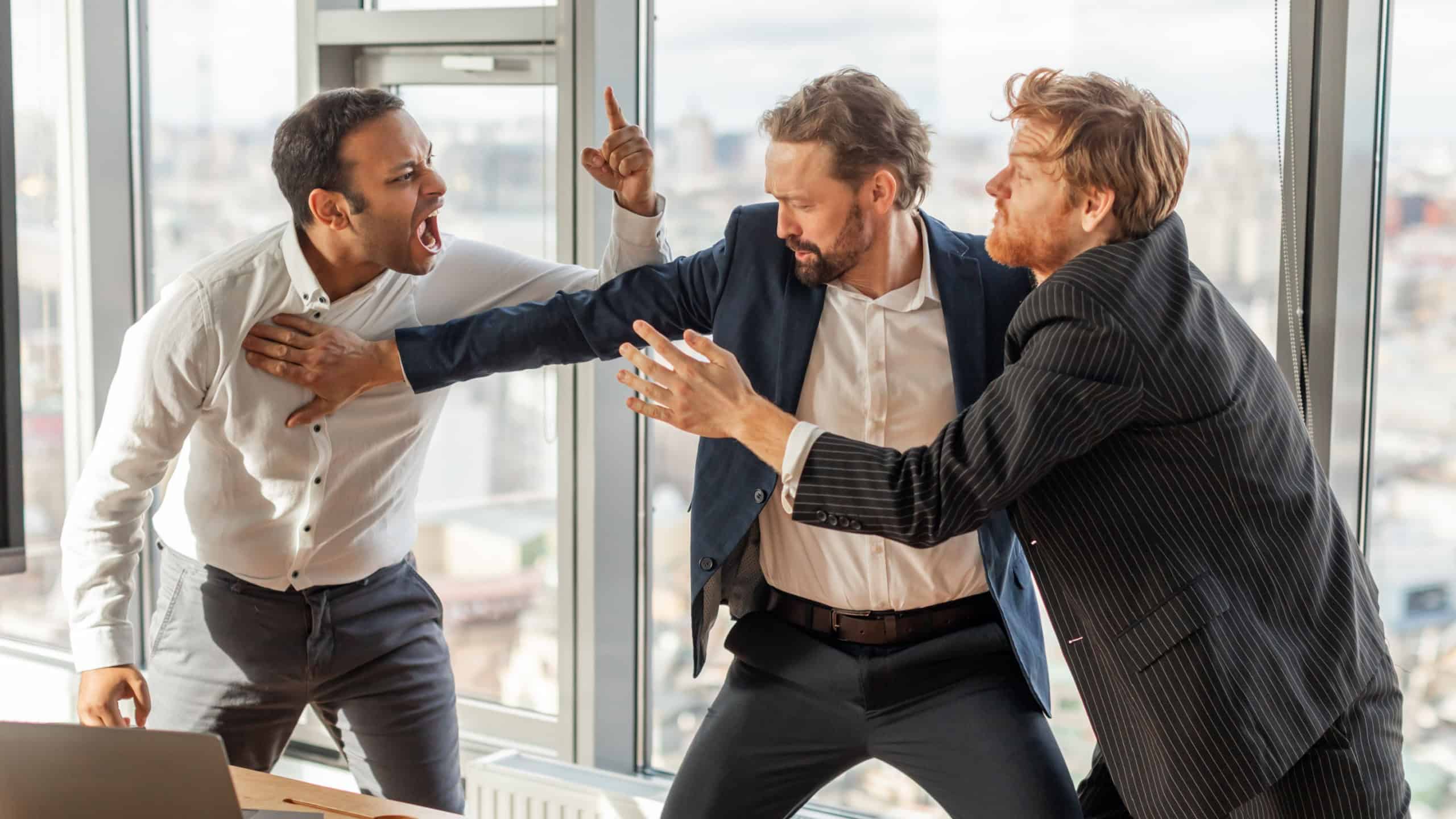 Three men in suits are engaged in a heated argument in a modern office setting. The man in the white shirt is yelling at the man in the blue suit, who is pushing him away