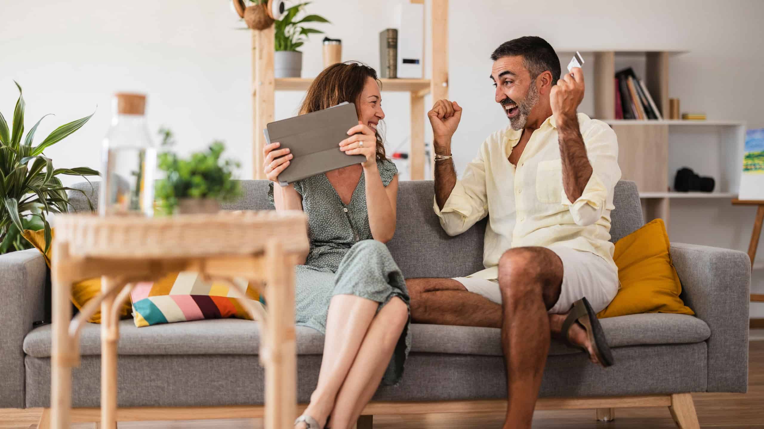 Mature couple happily shopping online with a tablet and credit card in their cozy living room, celebrating success and financial freedom