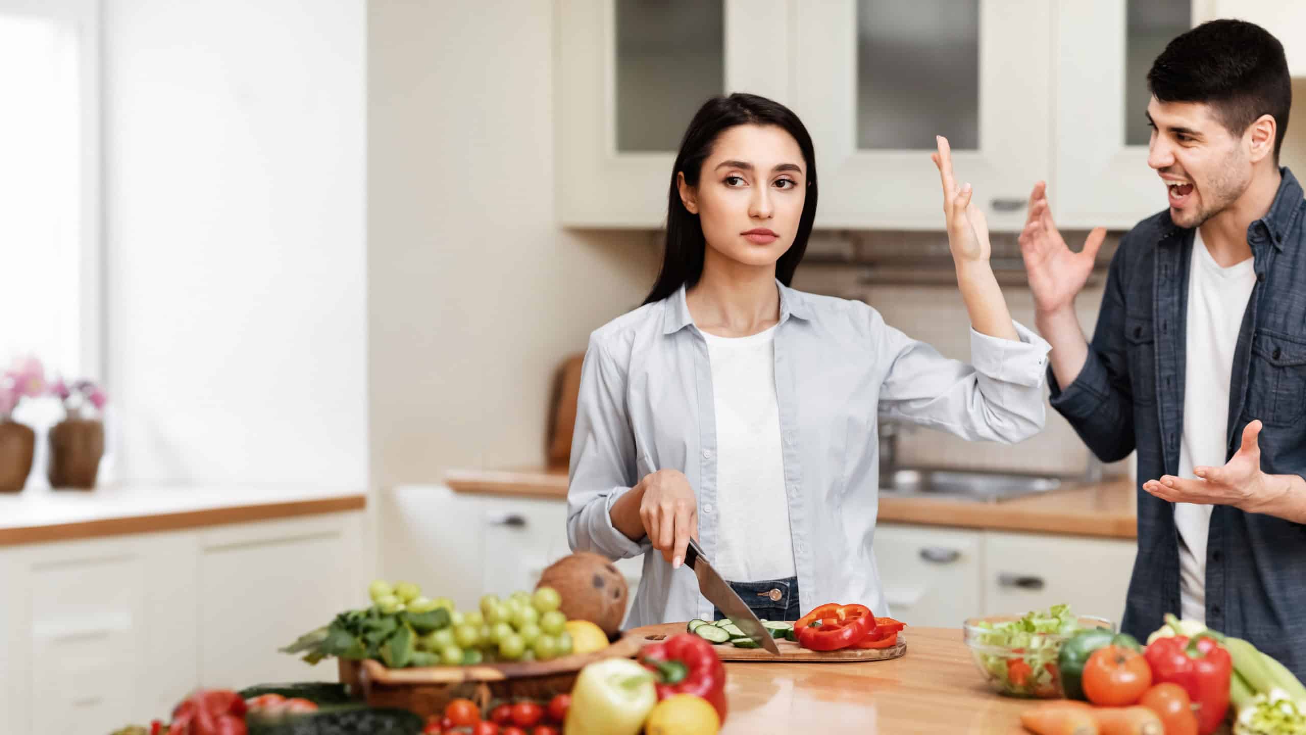 Family Problems Concept. Young couple arguing in the kitchen, man screaming, woman stopping him, showing palm