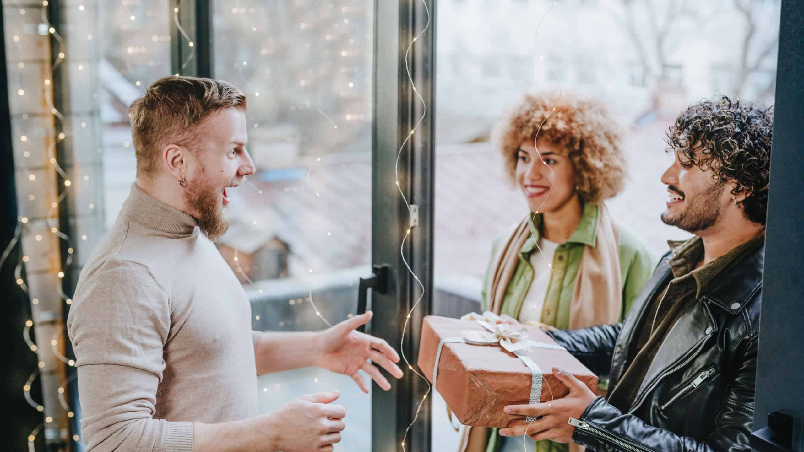 Man welcoming guests on holiday with gifts near door at home. Holiday time concept.