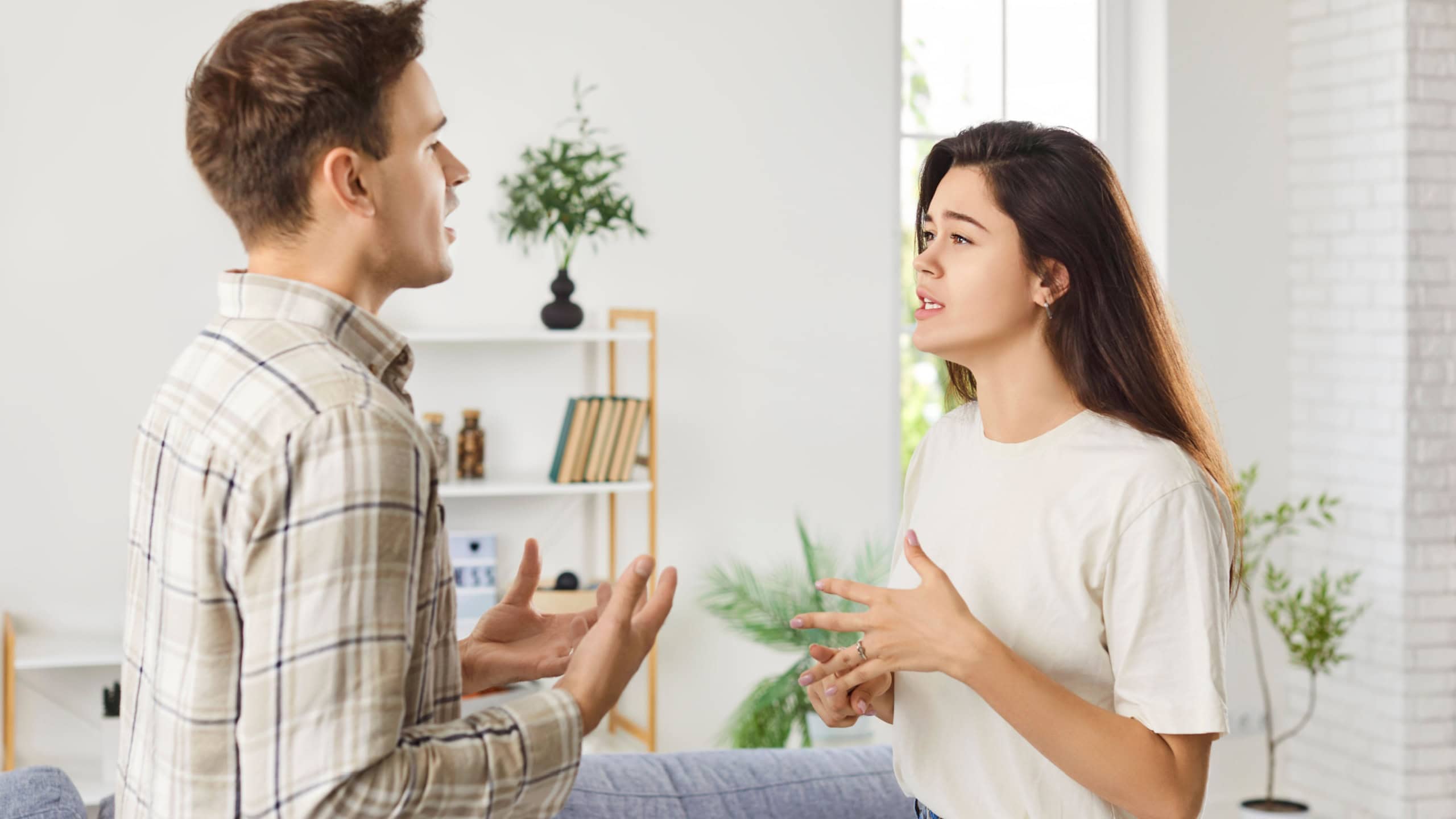 Frustrated unhappy husband and wife standing in the living room and quarreling. Angry stressed family couple arguing, shouting and interrupting each other, having relationship and marriage problems.