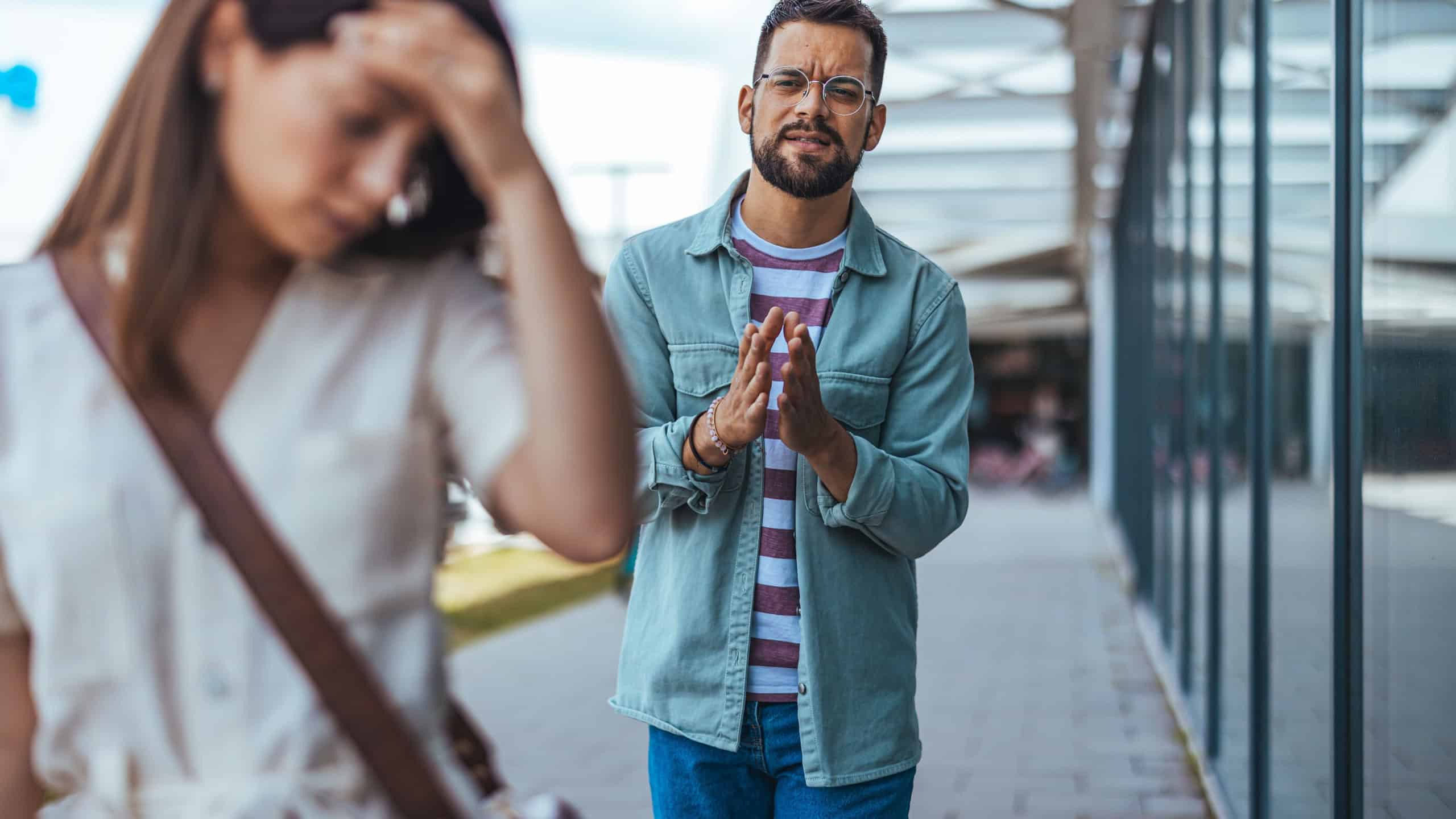 A frustrated woman walking away from a man amidst a disagreement in a city environment, emotions evident on her face. Captures dynamic themes of conflict, expression, and urbanization.