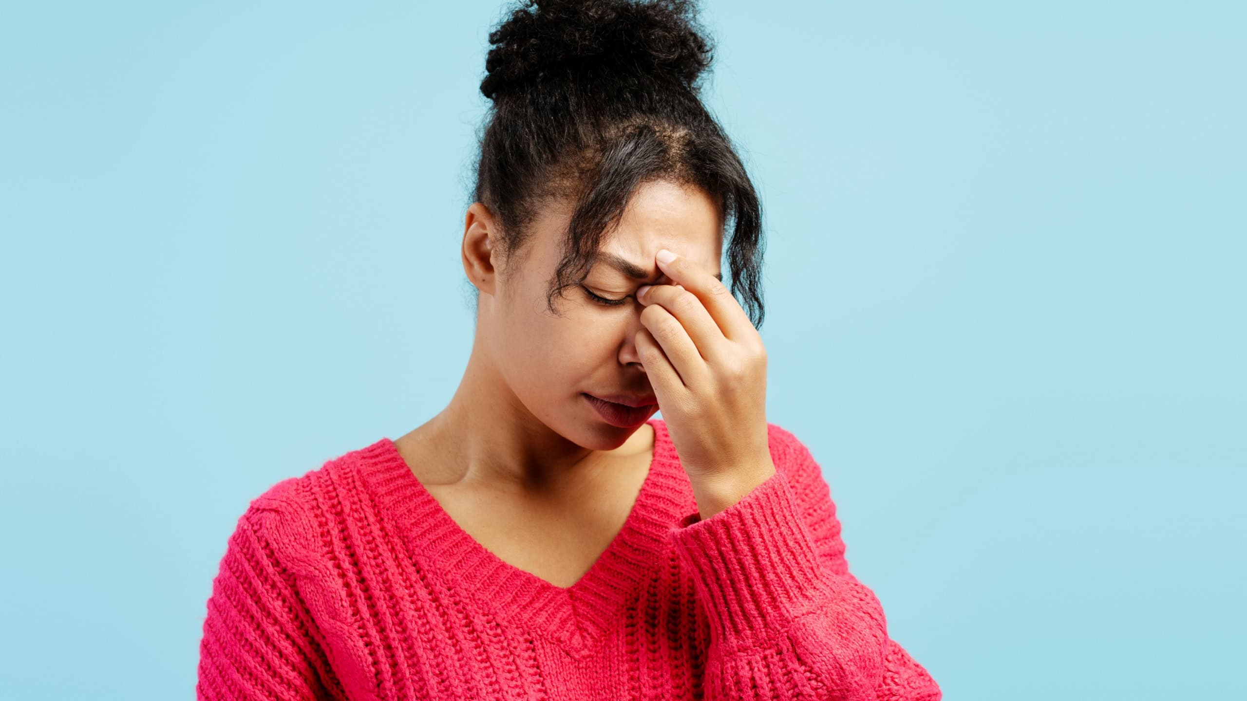 Studio portrait of a young woman touching her nose and suffering from sinus pain against a blue background
