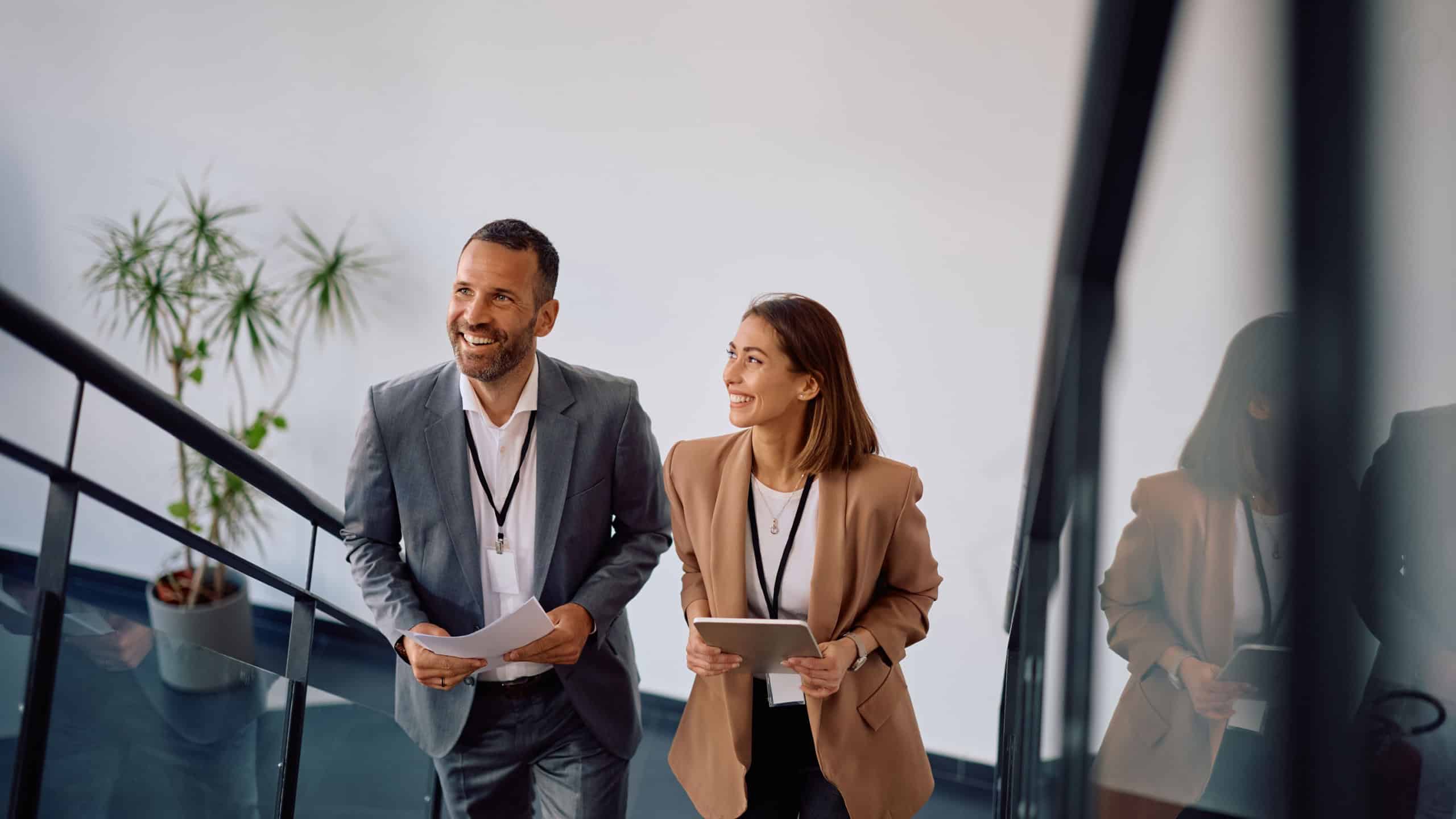 Happy businesswoman and her coworker moving up the stairs in the office. 