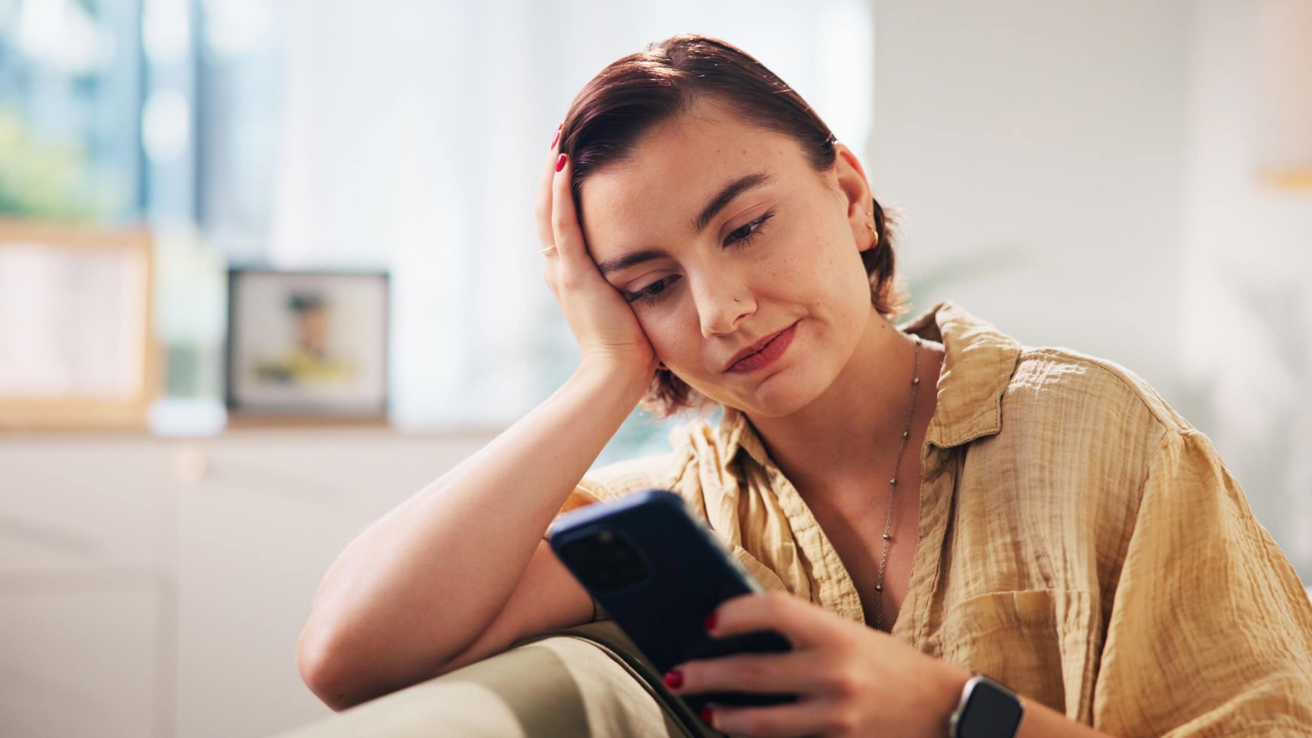 Woman, phone and bored on sofa in home, texting and check notification on web in living room. Person, smartphone and relax with chat, dating app and scroll on social media in lounge at apartment