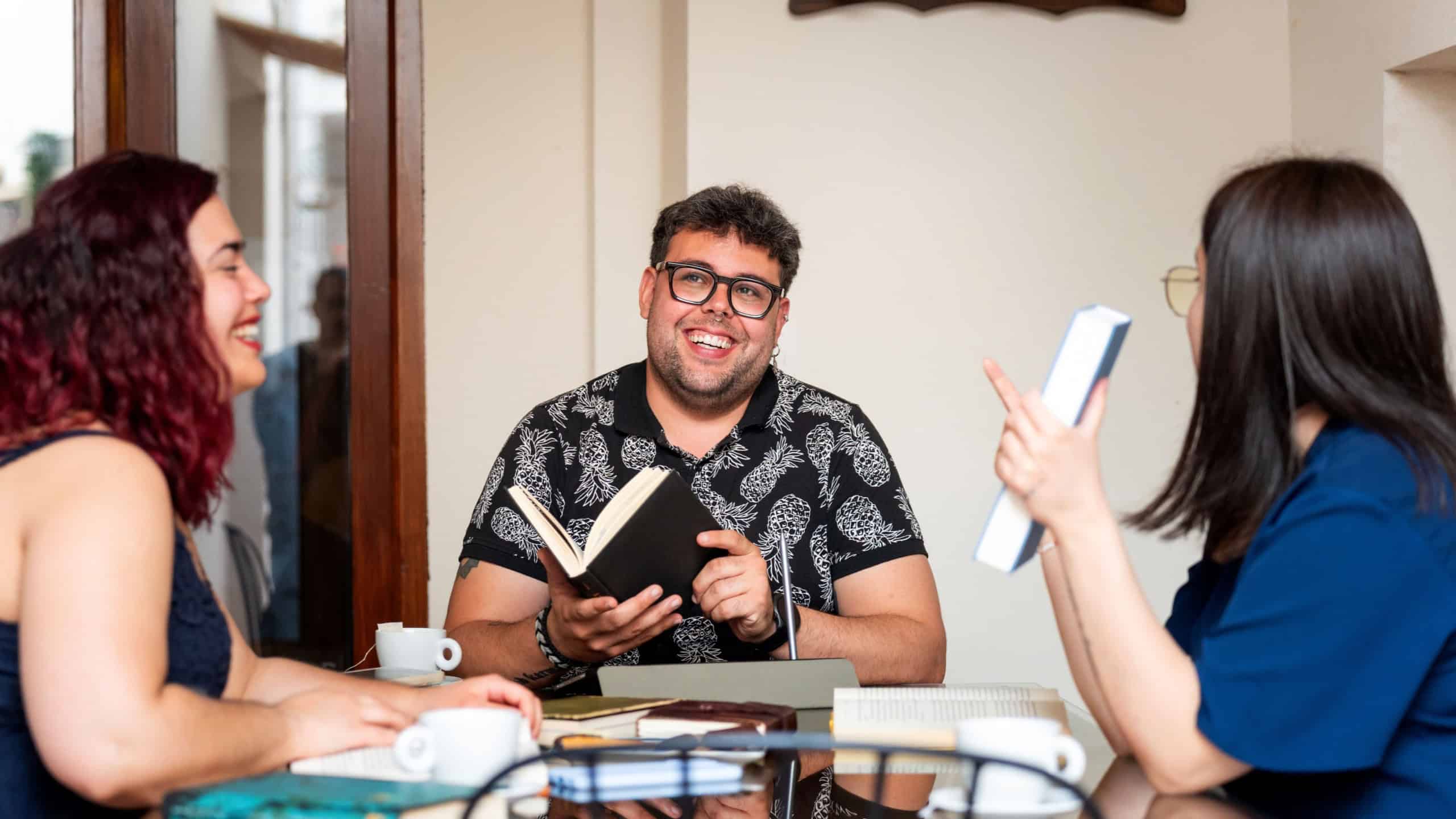 Smiling friends enjoying a book club meeting at a cafe, discussing literature and sharing their thoughts