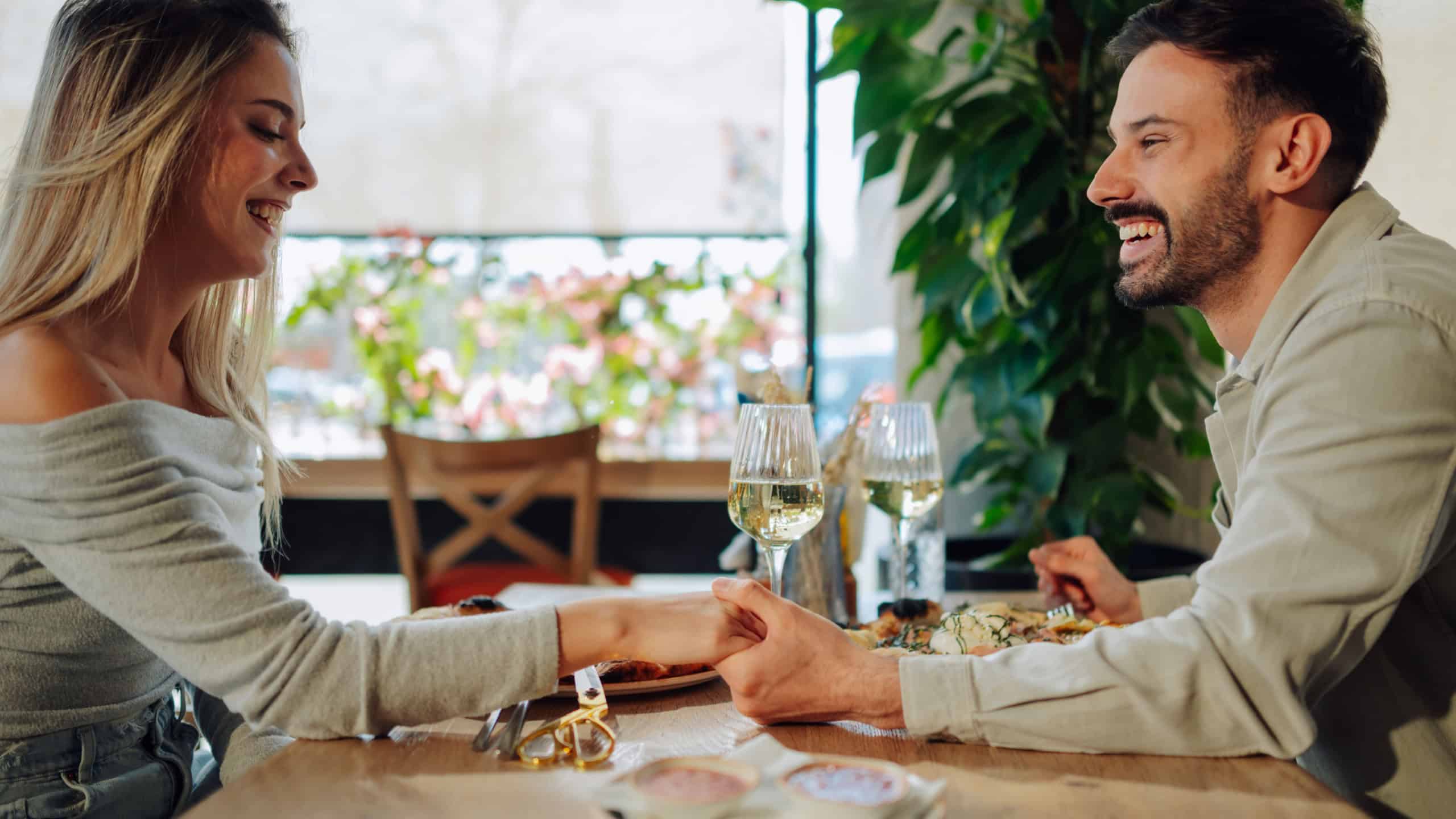Young loving couple holding hands and smiling while having romantic lunch together in a restaurant