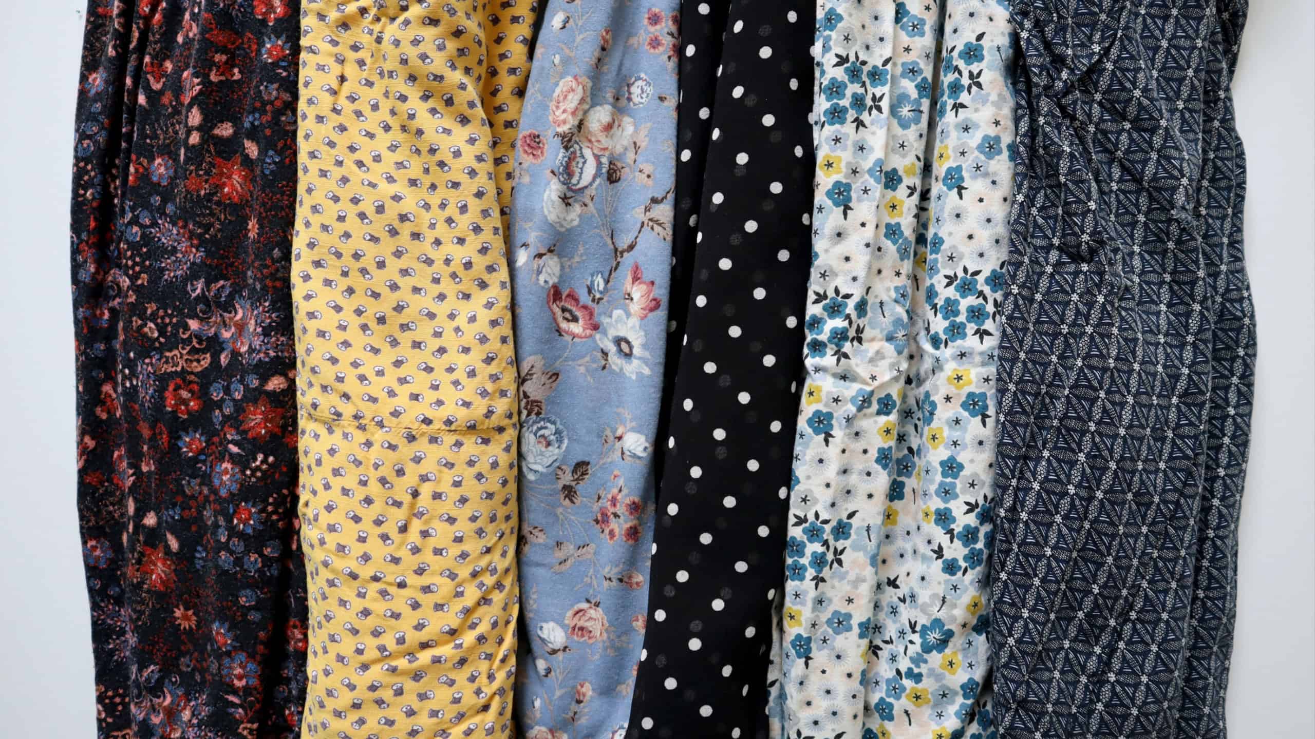 Photo of various printed fabrics. Arranged in vertical stripes on white background. Different colors and patterns. Floral prints, polka dots, ornaments. Blue, yellow, brown, white, black. Clothing.