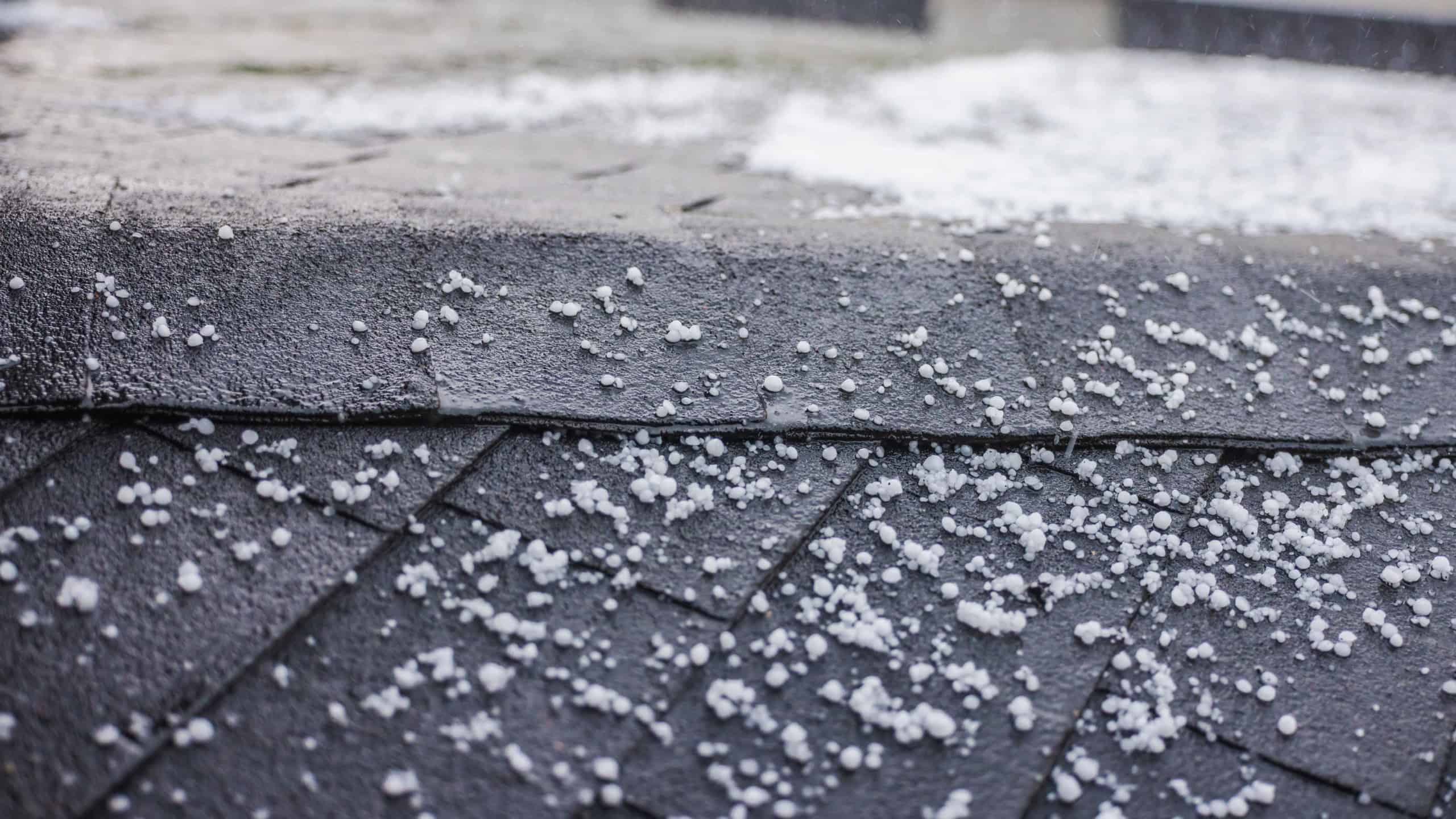 Small hailstones scattered on a dark shingled roof during a rainstorm.