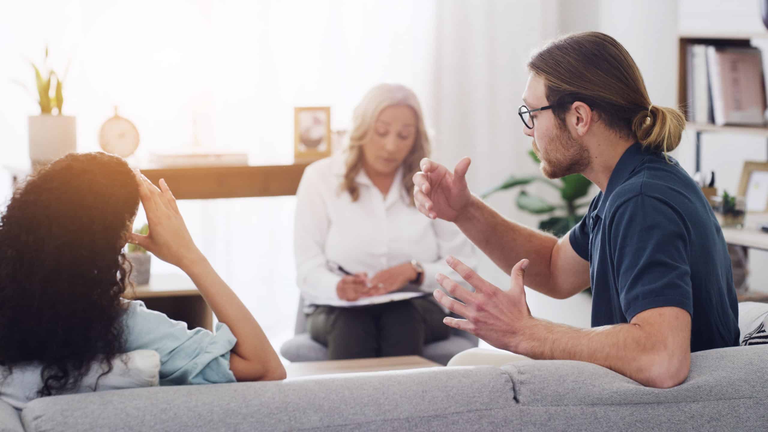 Couple, therapist and argument on sofa, fight and consultation for mental health at wellness clinic. People, psychologist and writing notes on clipboard, stress or conflict resolution in relationship