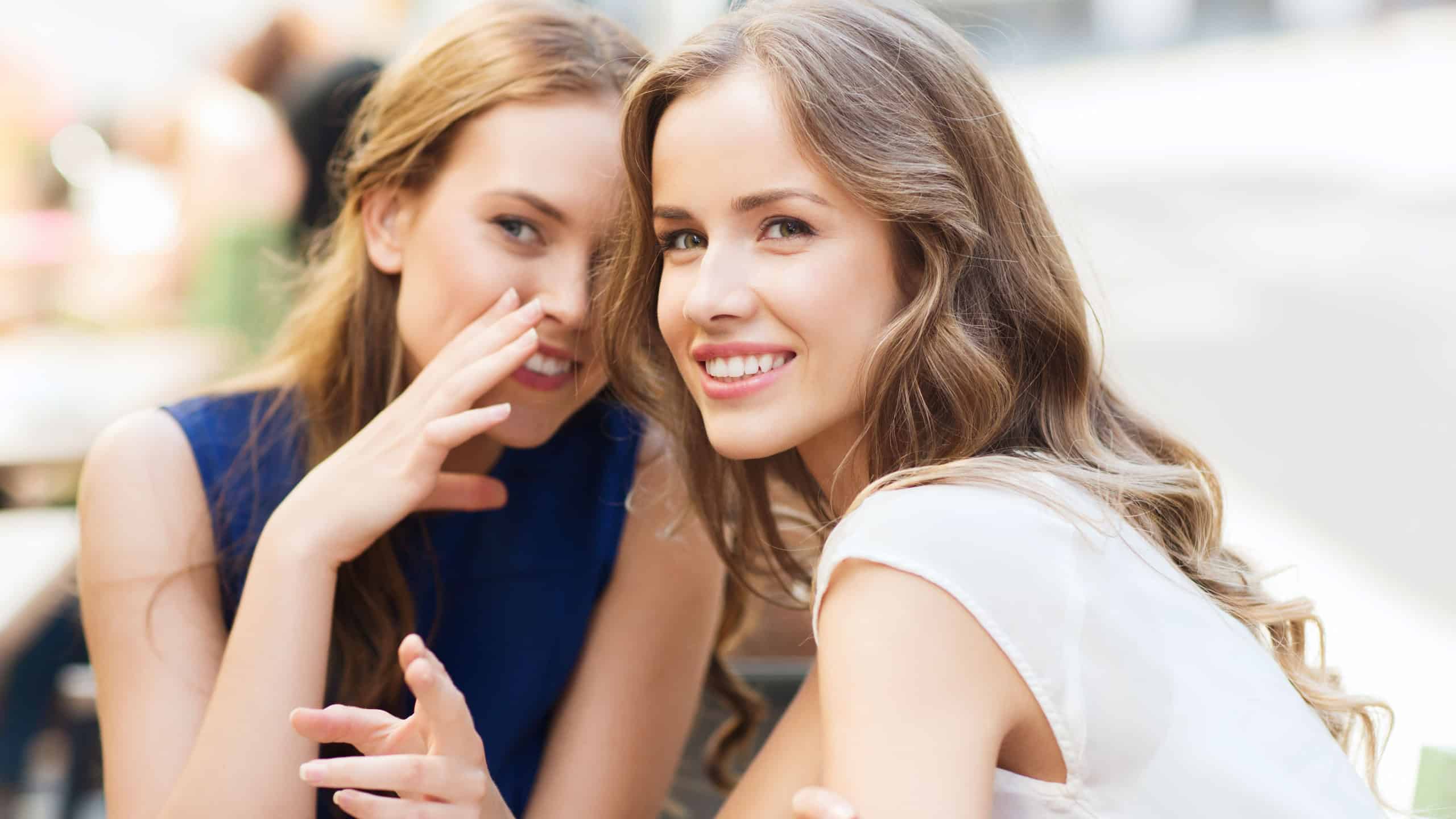People communication and friendship concept - smiling young women drinking coffee or tea and gossiping at outdoor cafe
