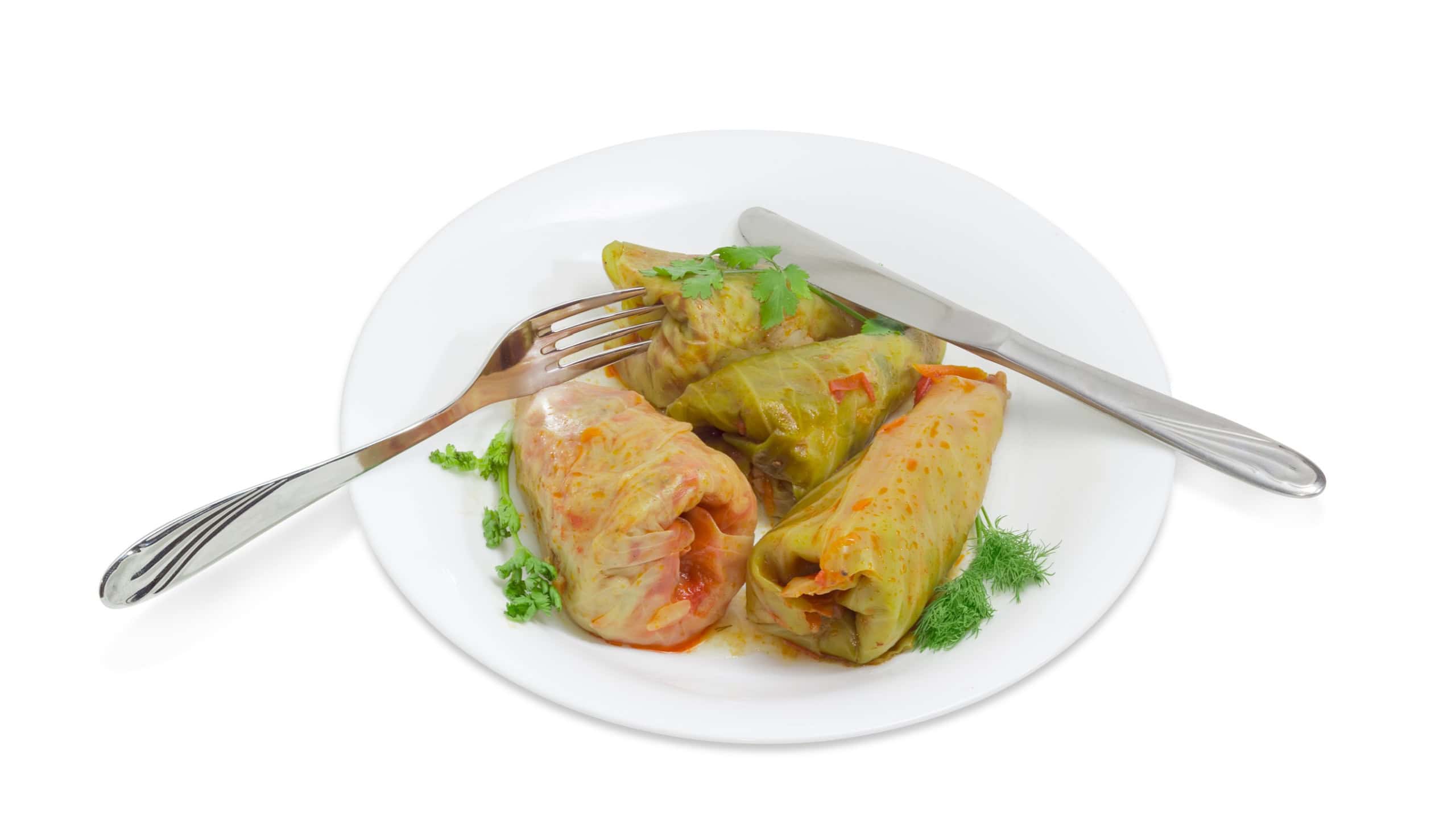 Several cooked cabbage rolls, twigs of greenery, fork and knife