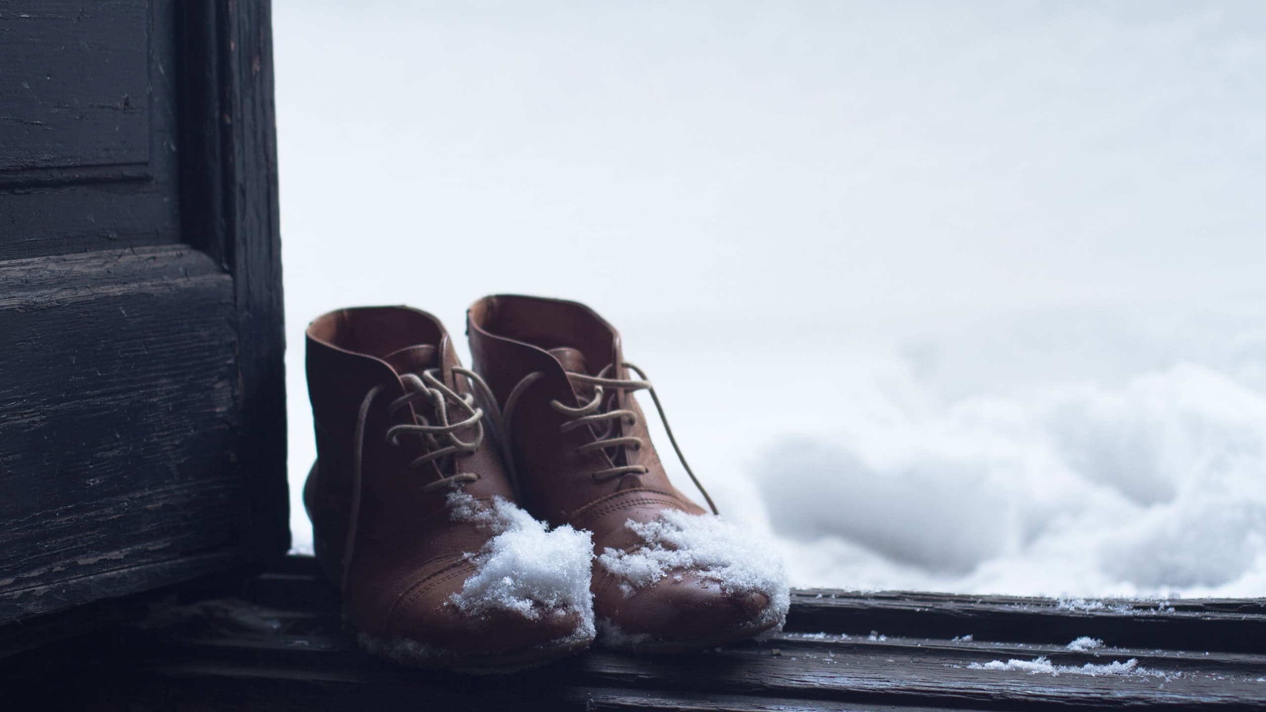 Front view of a pair of vintage brown leather shoes by the house wooden open door entrance covered in snow in winter time
