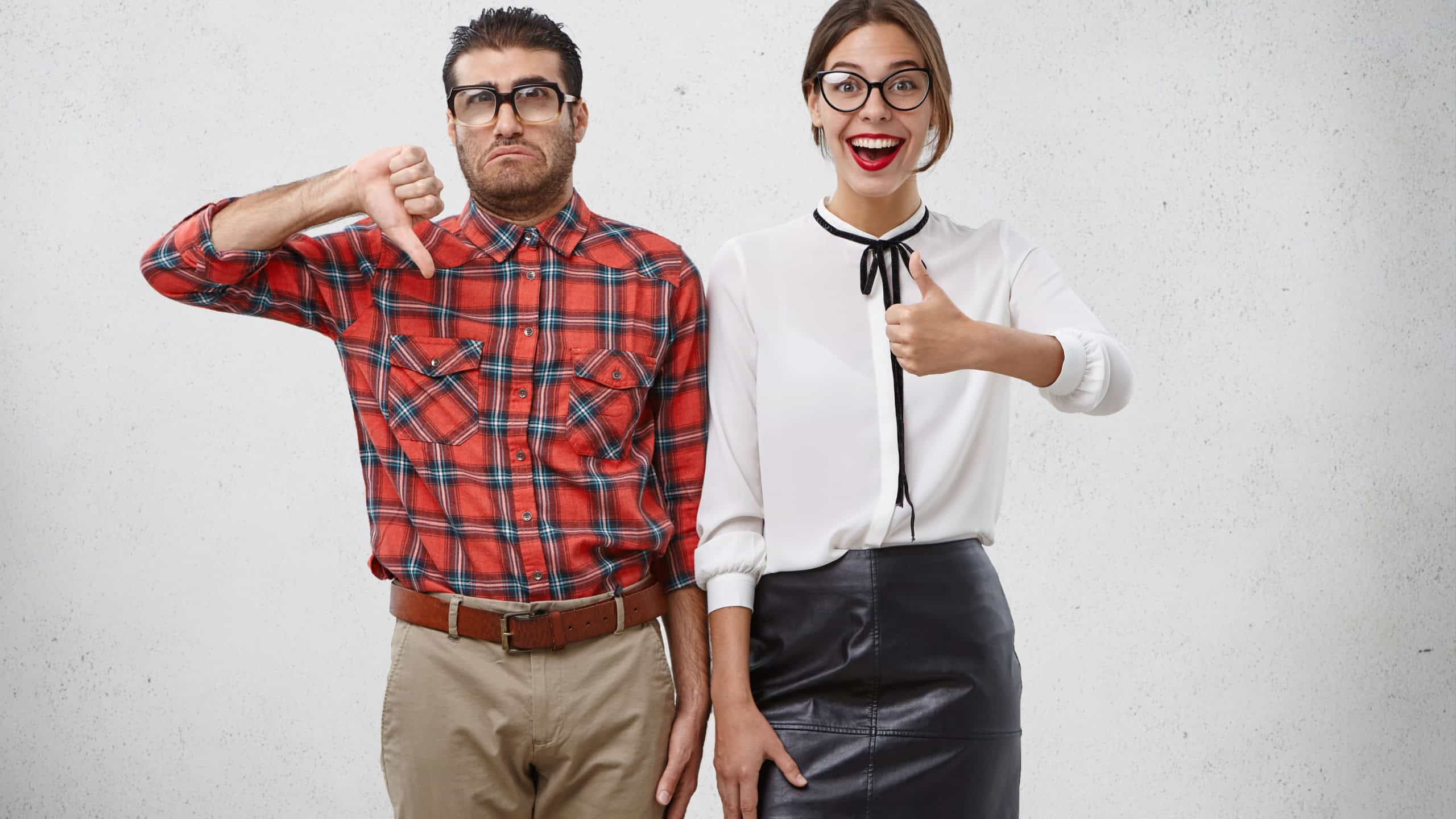 Depressed man shows dislike sign, being tired of work, looks unhappily stands near woman with happy expression, have opposite reaction on proposal. Emotional weird couple express different opinion