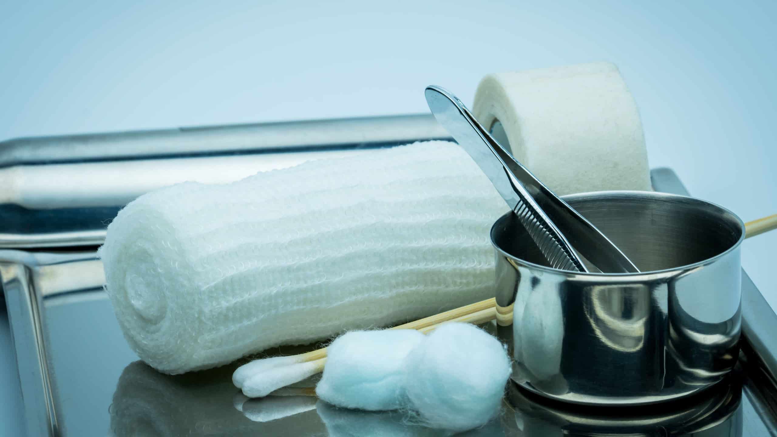 Wound care dressing set on stainless steel plate. Cotton ball with alcohol, cotton stick, surgical tape, forceps and conform bandage.