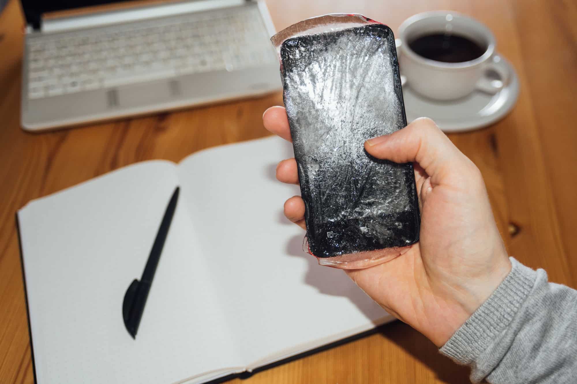 Frozen phone in man hand. Cold call concept. Desk on background