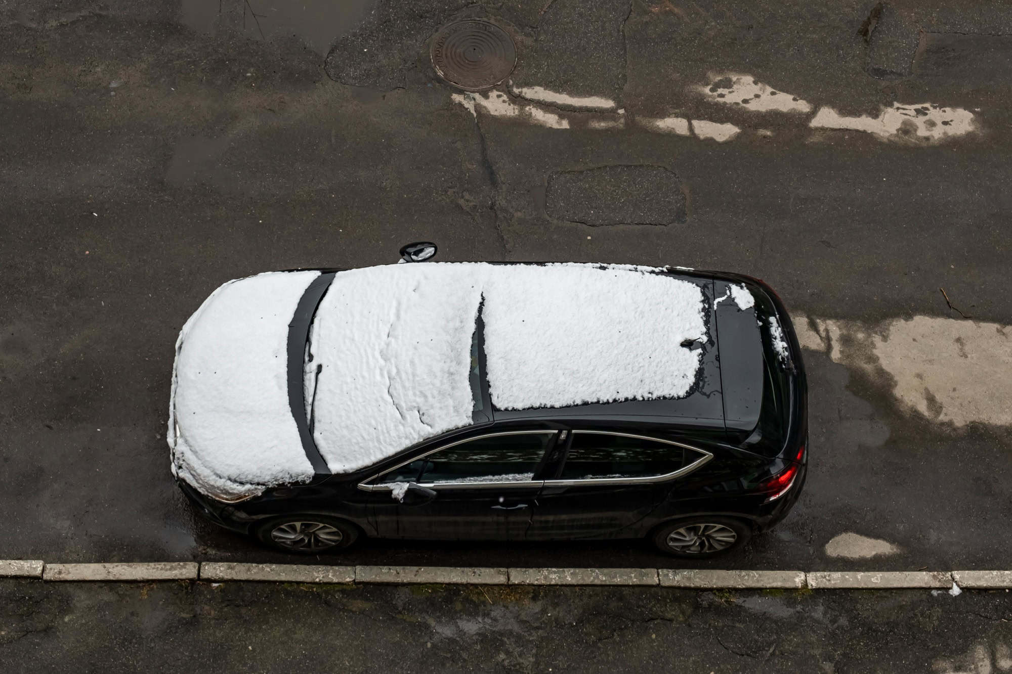 Ukraine, Vinnitsa, November 5, 2019. Cosmonavts Street 65 . A car covered in the first snow parked near a multi-storey. Top view.