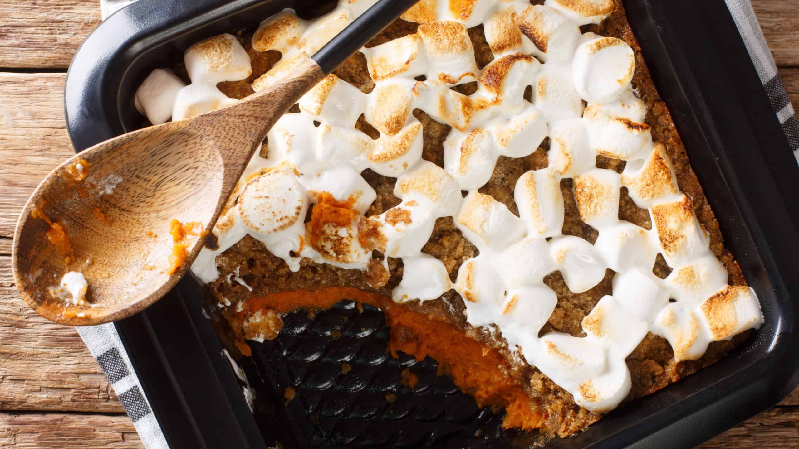 Sweet potato casserole with pecans topped with marshmallows close-up in a baking dish on the table. Horizontal top view from above