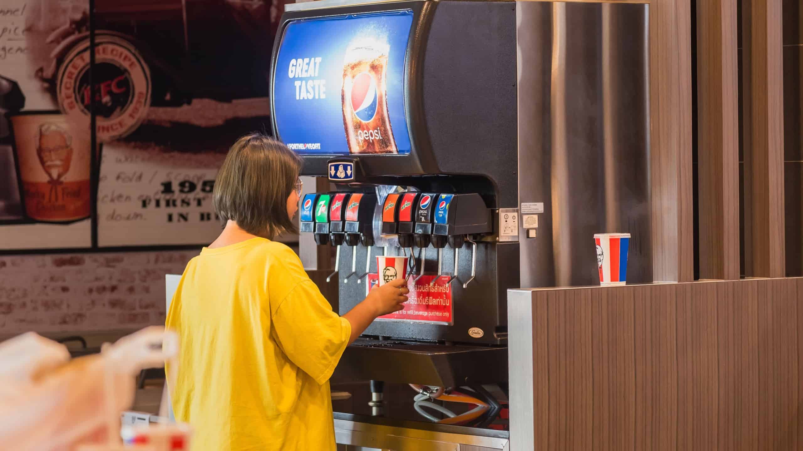 Bangkok, Thailand - April, 08, 2020 : Unknown name woman is pressing soft drinks from pepsi machine for refill self service in Kentucky Fried Chicken or KFC fast food restaurant in thailand.