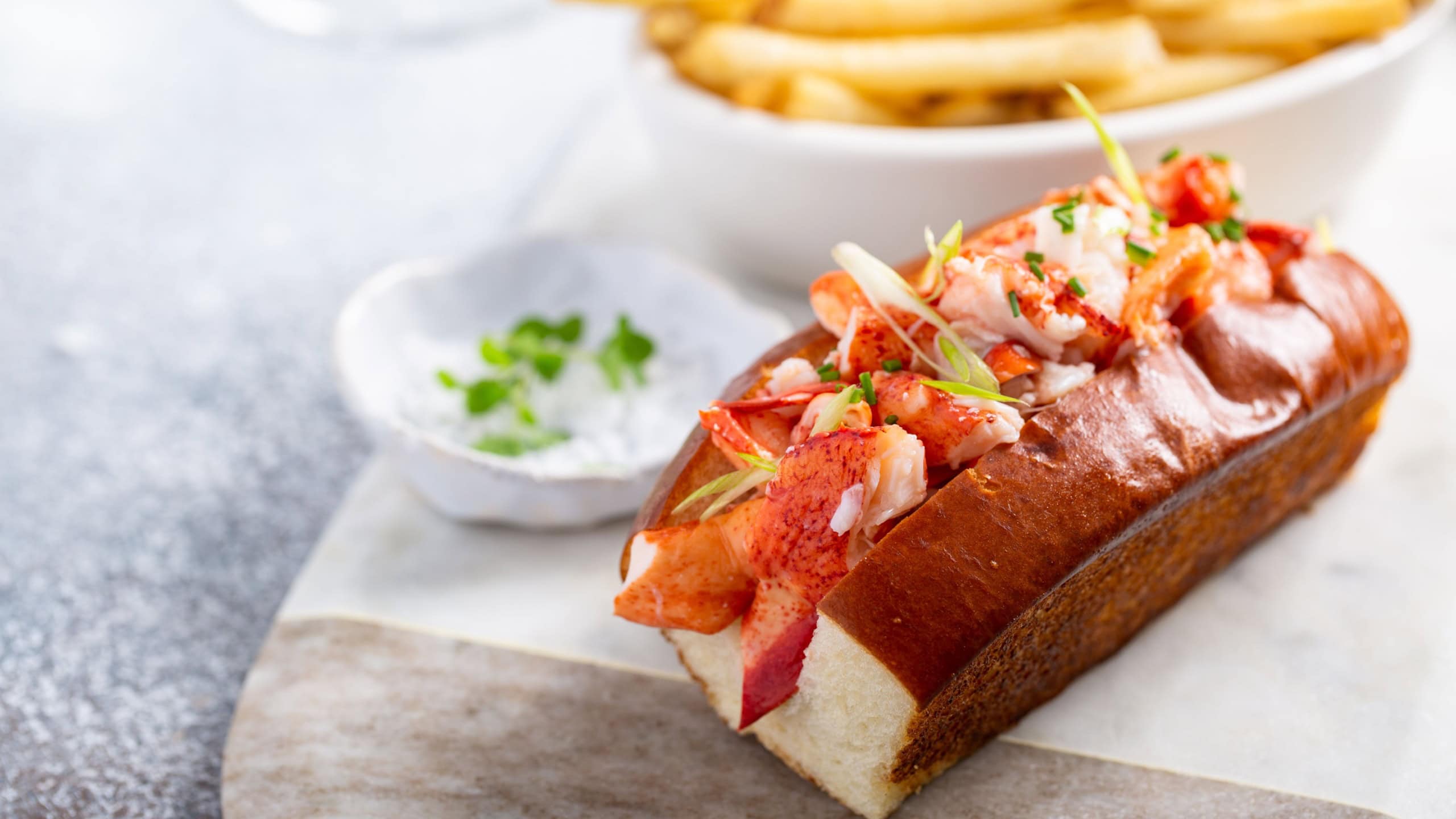 Lobster roll on a brioche bun with fries on a marble board