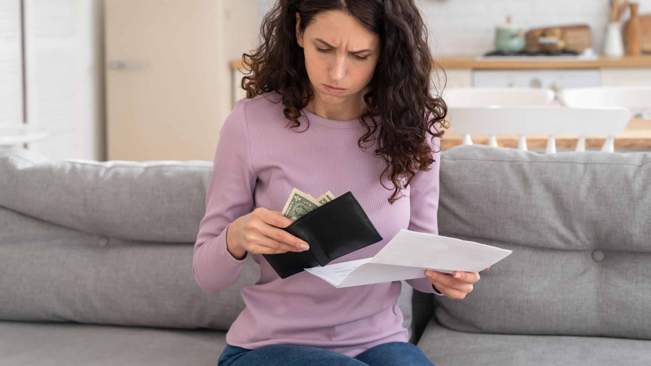 No money left. Unhappy sad girl holding last cash money in wallet, papers calculate domestic bills at home. Millennial woman frustrated about lack of finances, feeling anxiety about debt or bankruptcy
