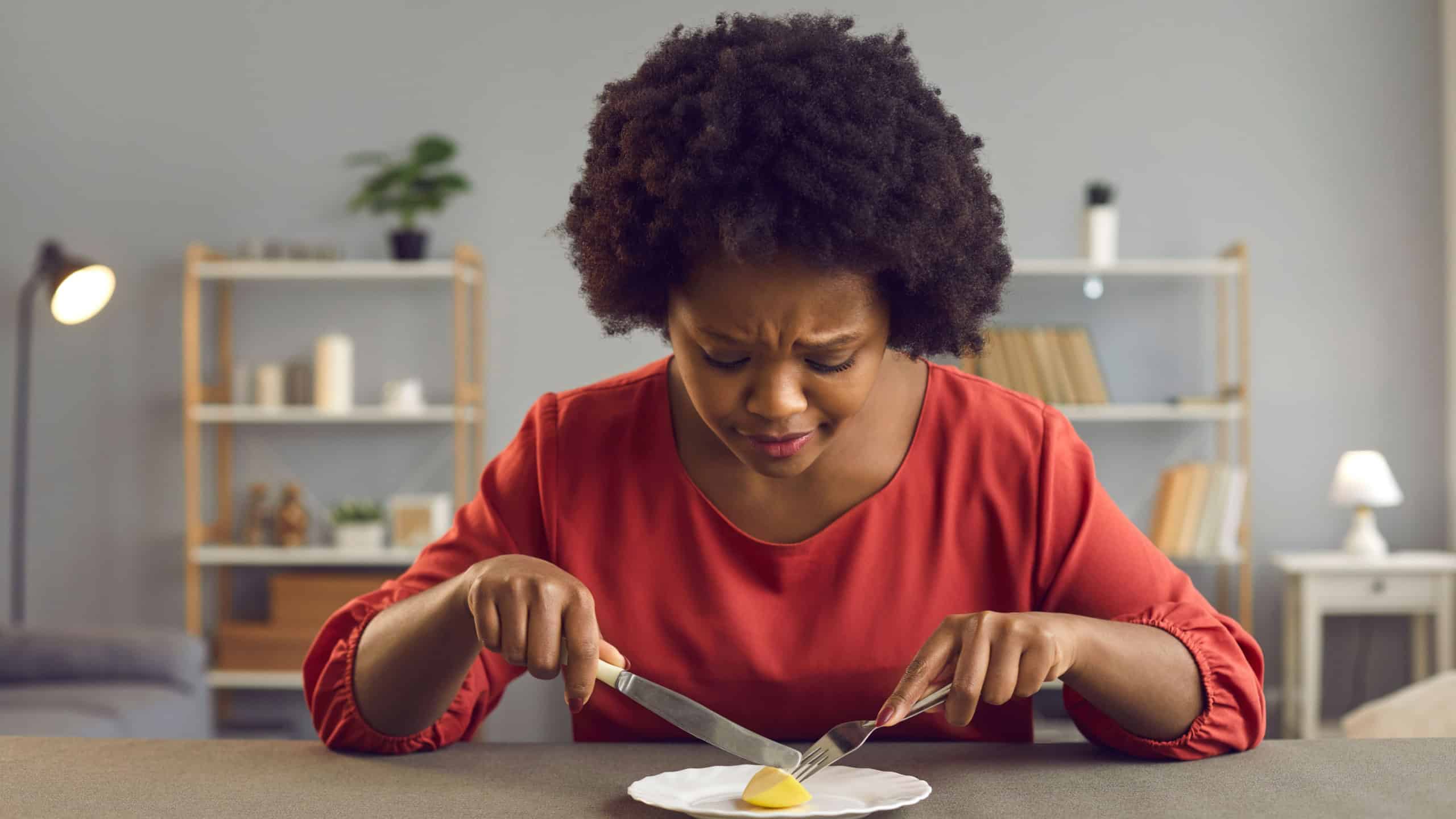 Young lady having tiny serving for lunch. Sad black woman who's sticking to strict diet eating nothing more than ridiculous portion of one little piece of apple. 