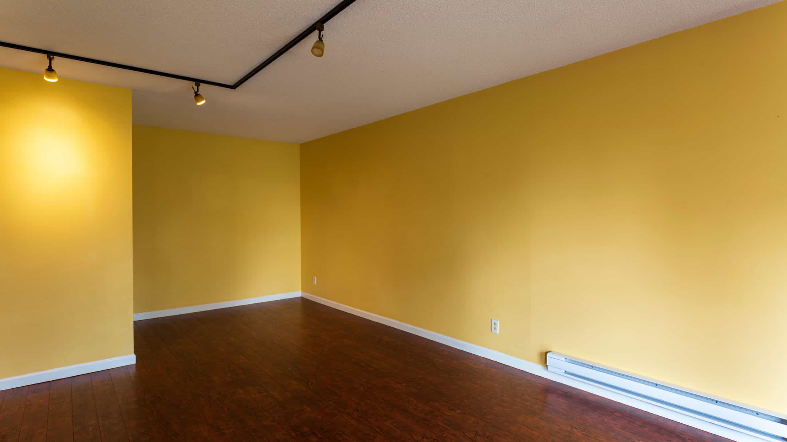 View of empty living room in a modern new apartment condo house interior with empty yellow walls. Baseboard heater near footboard.