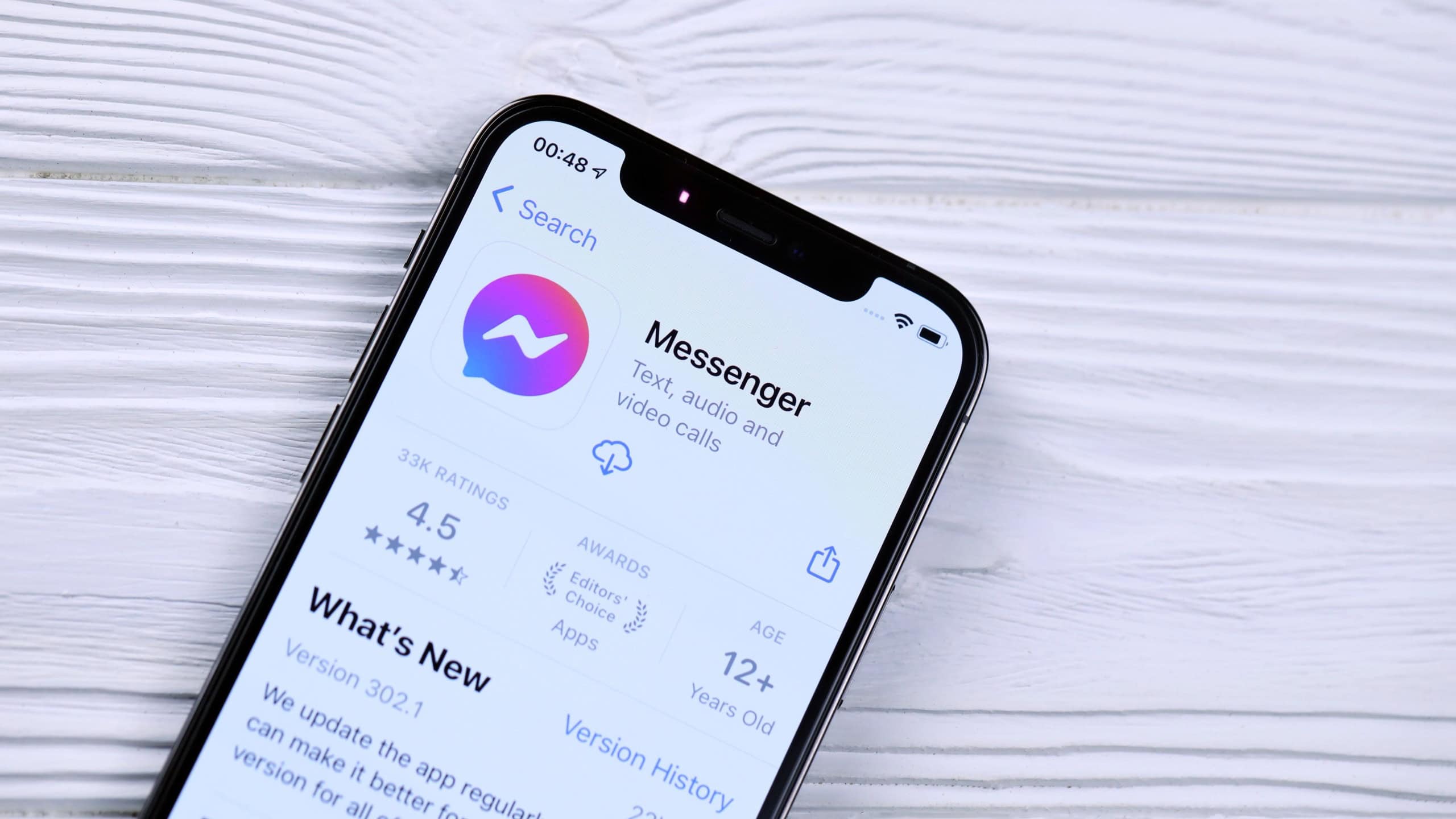  Facebook messenger icon and application from App store on iPhone 12 pro display screen on white wooden table