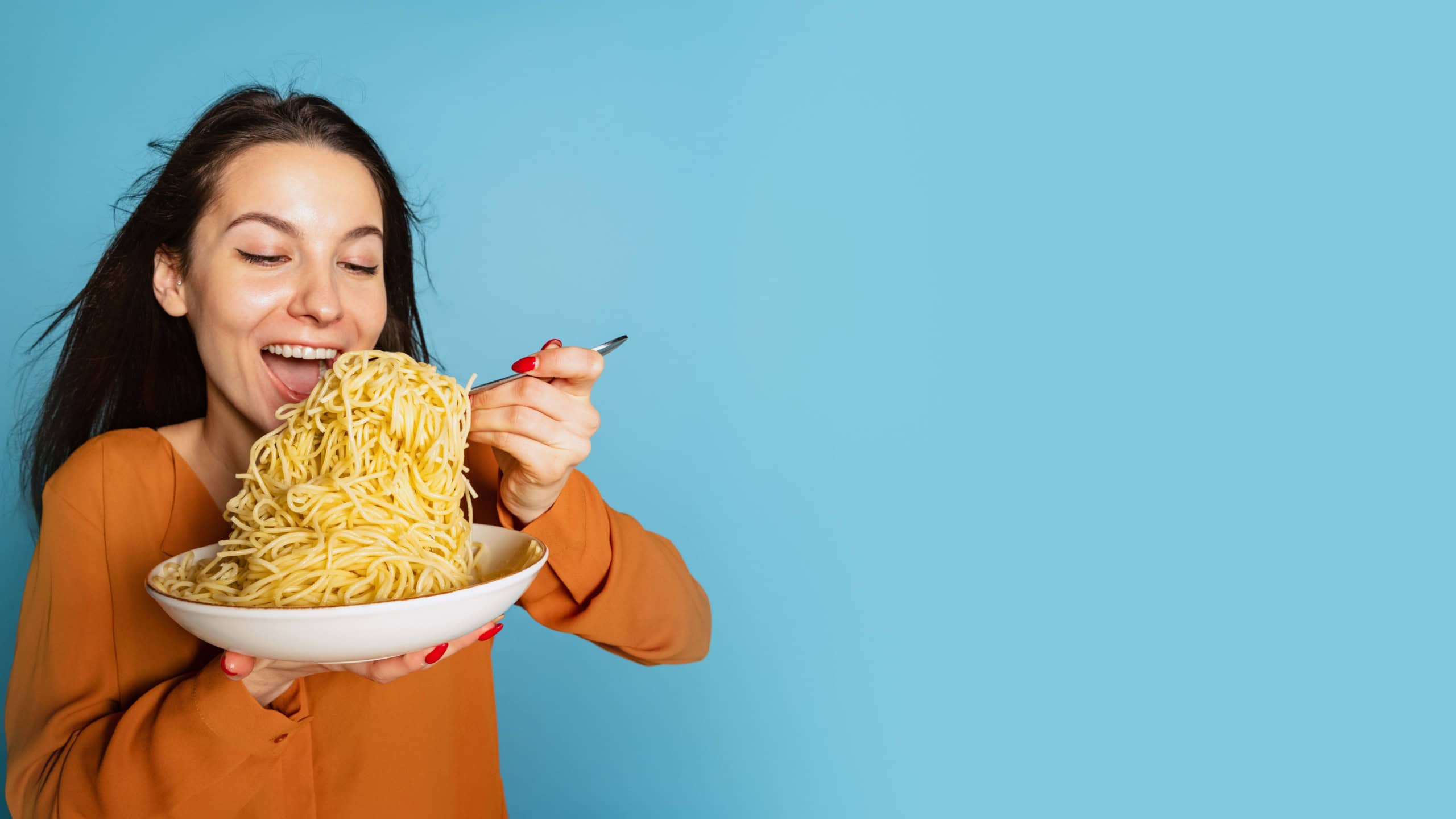 Excited young girl preparing to eat large portion of noodles isolated on blue studio background. Holidays, traditions, food, popularity, taste and love. healthy carbohydrates.