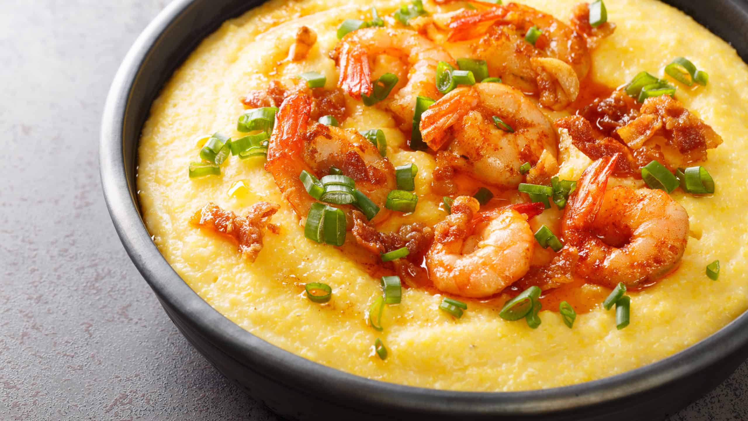 Bowl with fresh tasty shrimp and grits on a dark concrete background. American cuisine. Horizontal