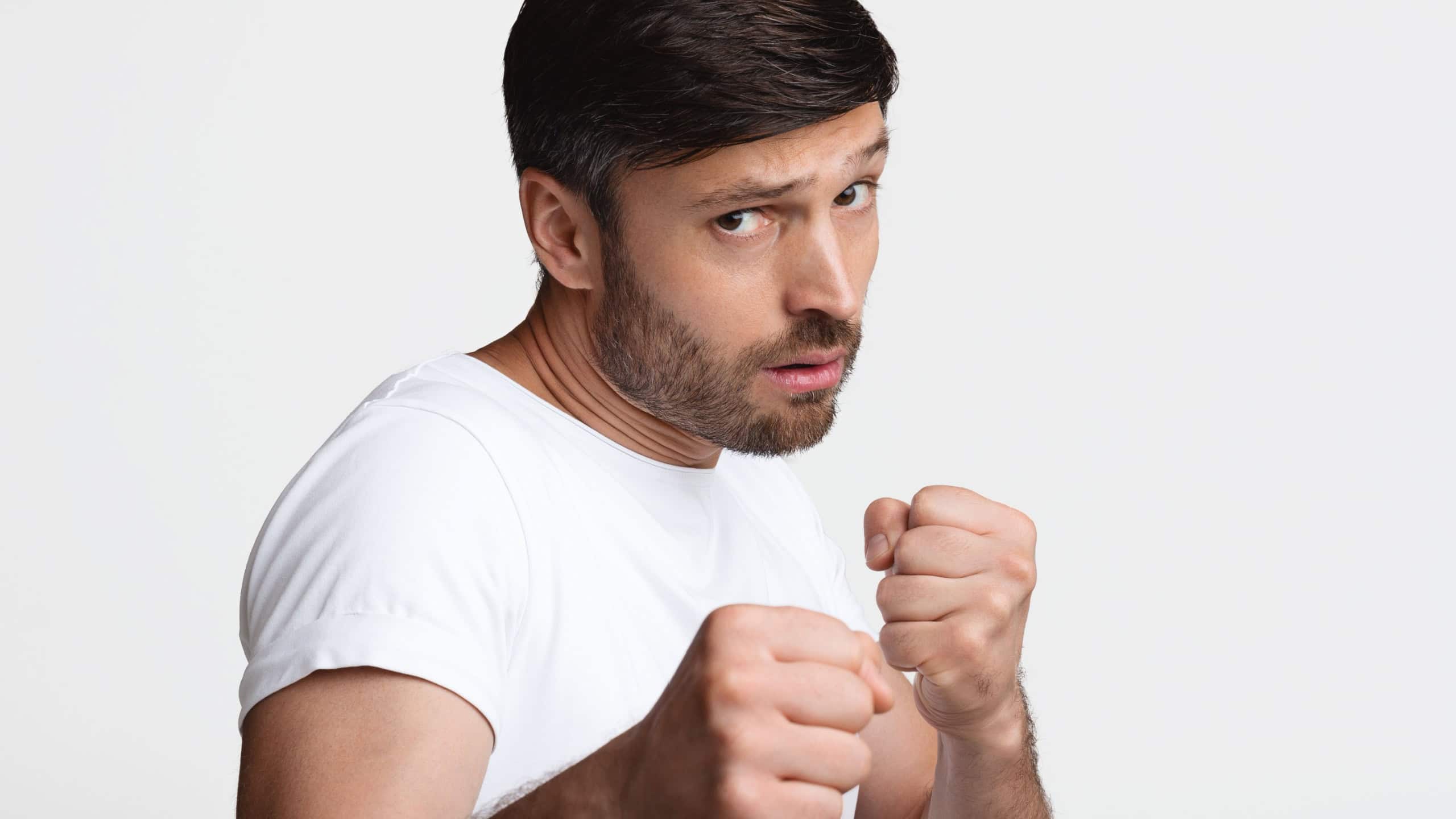 Determined Man Clenching Fists Ready To Fight Standing Over White Studio Background. Confident Male Boxing Looking At Camera Seriously. Self Defence Concept
