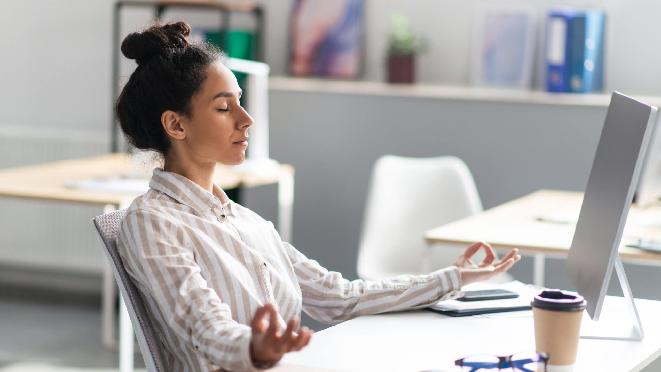 Coping with stress at work. Young latin office worker meditating at workplace in office after busy day, doing breathing exercises. Workplace stress management