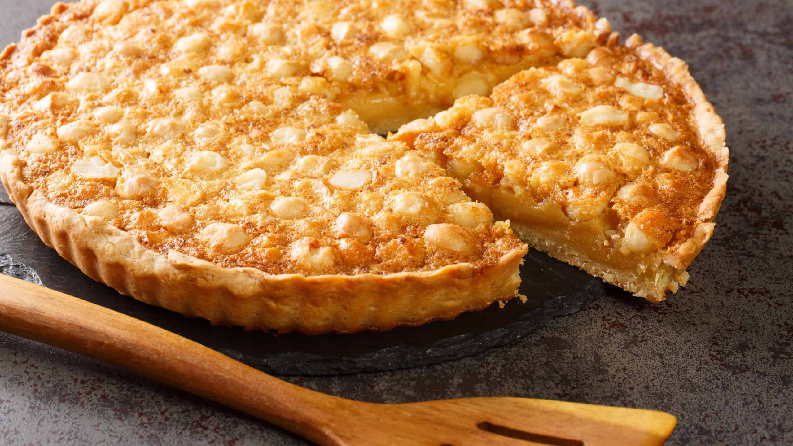 Caramel macadamia tart baked in a buttery homemade shortcrust pastry closeup in the board on the table. Horizontal