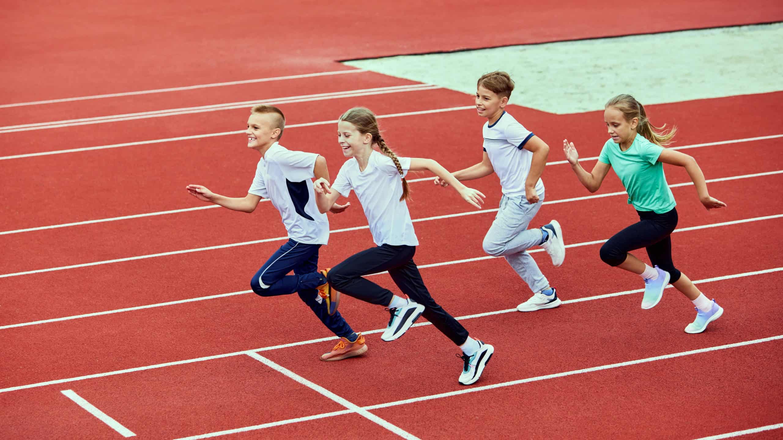 Group of children running on treadmill at the stadium or arena. Little fit boys and girls in sportswear training as athletes outdoor. Concept of sport, fitness, achievements, studying, goals, skills