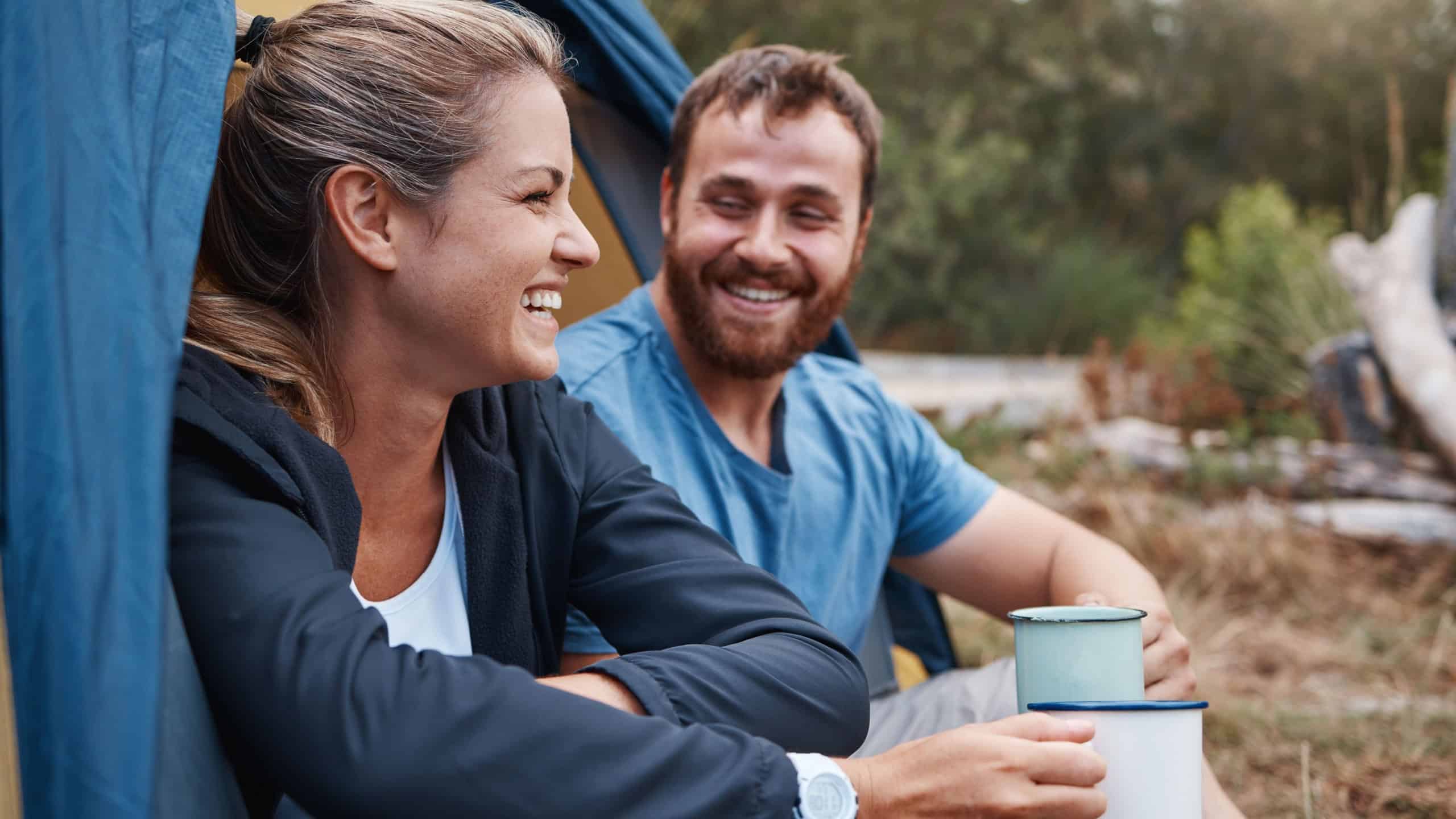 Couple, bonding or drinking coffee in camping tent in nature earth environment, Canada woods or sustainability forest. Smile, happy woman or laughing man with tea on romance love date in countryside