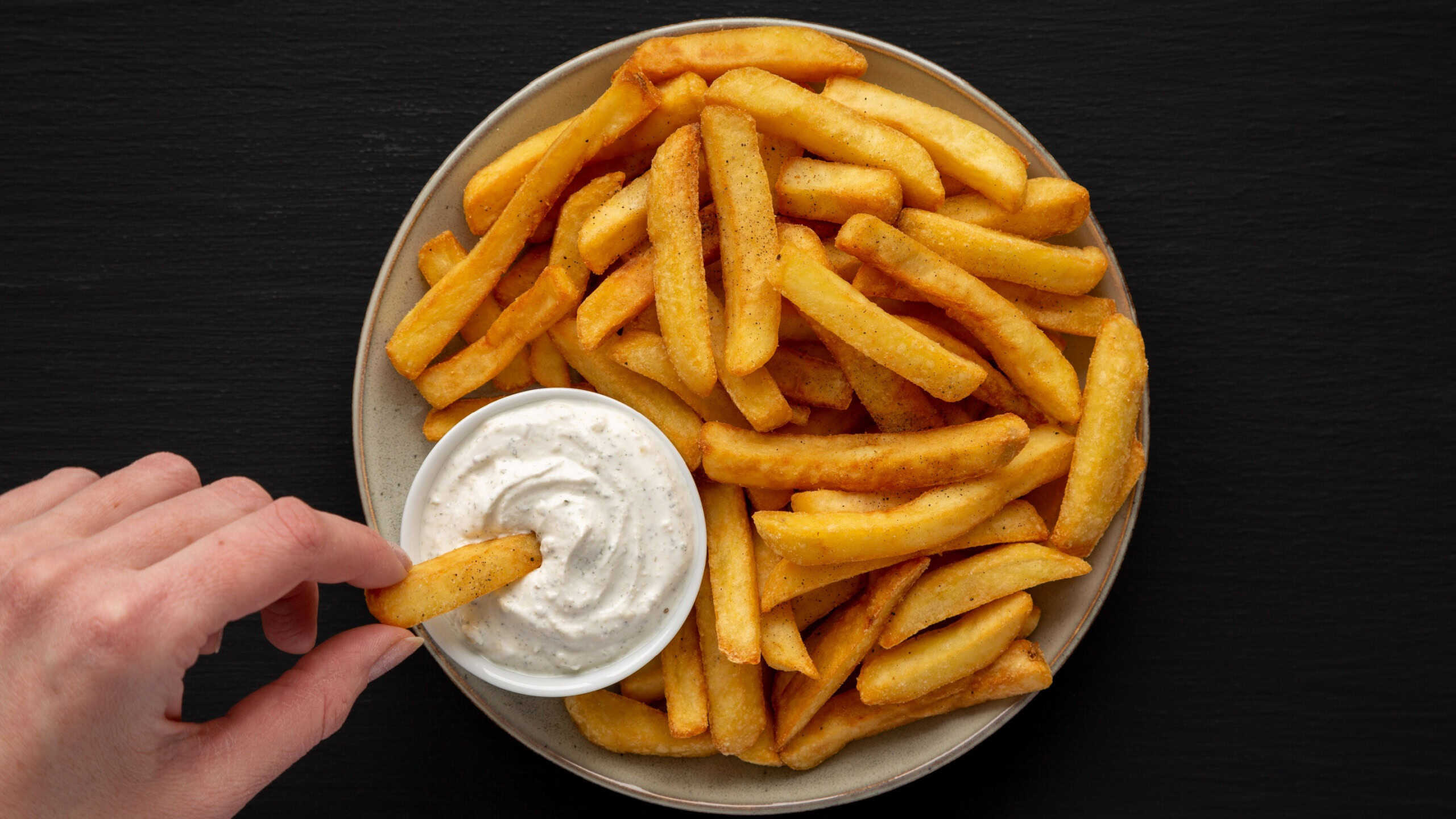 Hand takes French Fries with Ranch Dressing, top view.