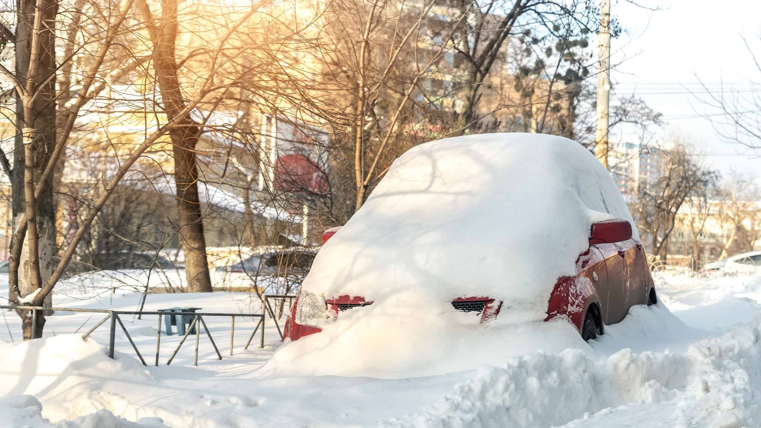 City street driveway parking lot spot with small car covered snow stuck trapped after heavy blizzard snowfall winter day by big snowy pile. Snowdrifts and freezed vehicles. Extreme weather conditions