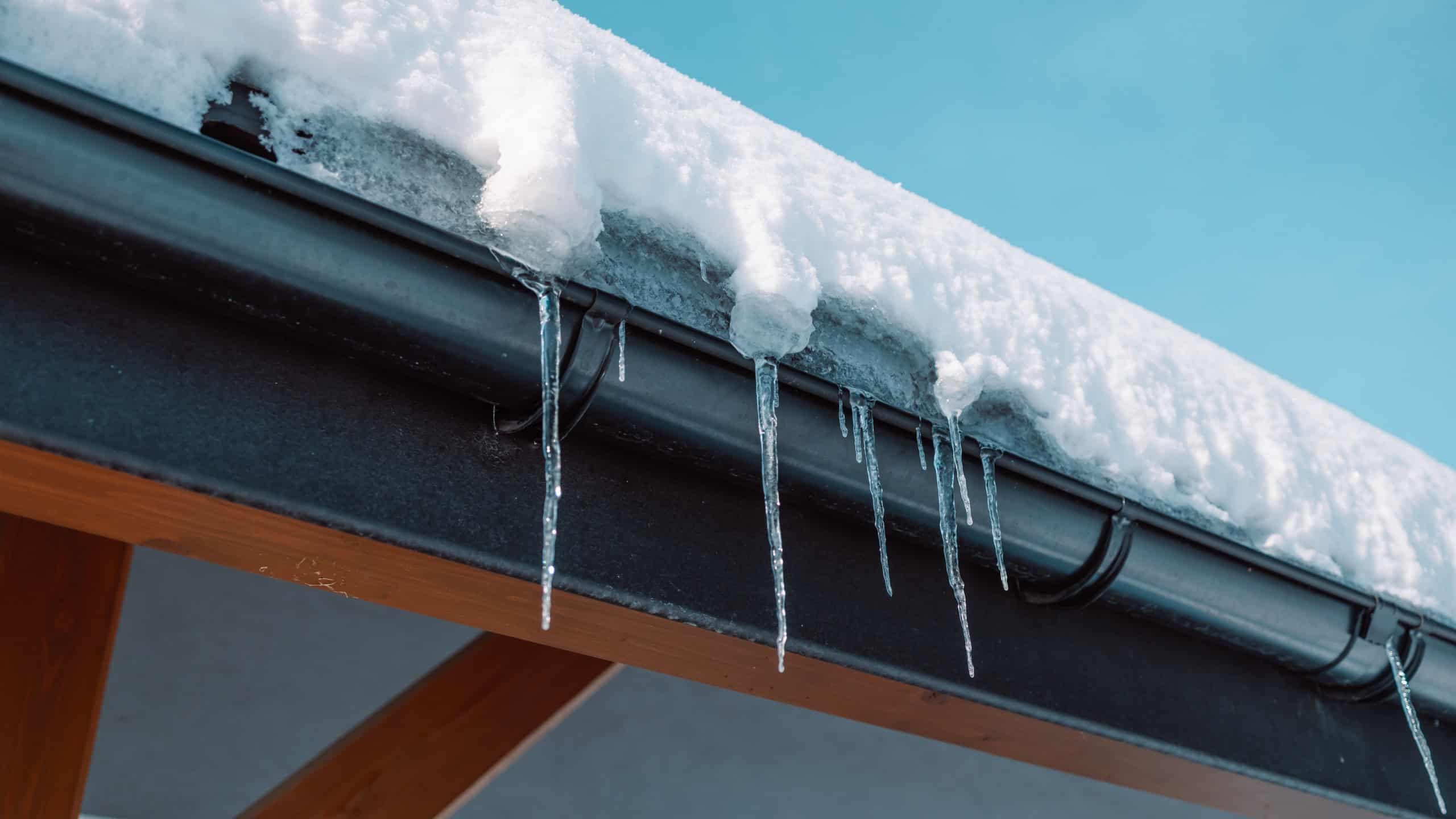 Icicles hang from the roof of a log house near which a car is carelessly parked, which can be damaged by falling ice floes.