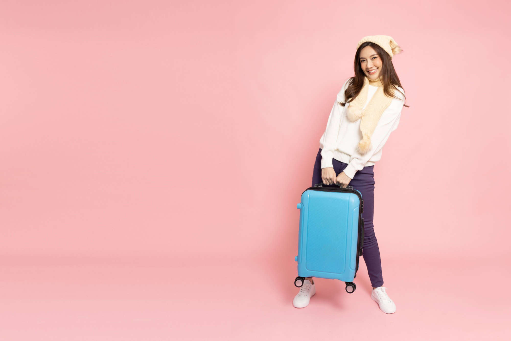 Happy Asian woman traveler holding luggage isolated on pink background, Tourist girl having cheerful holiday trip concept, Full body composition