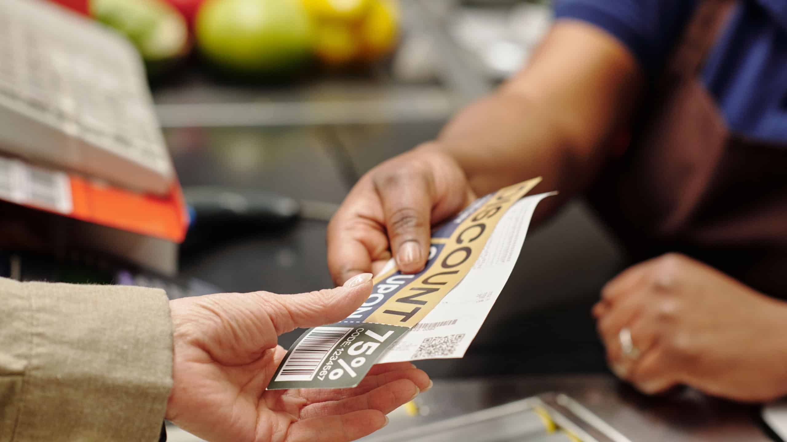 Hand of young African American female cashier passing discount coupon and receit to customer over checkout counter in supermarket