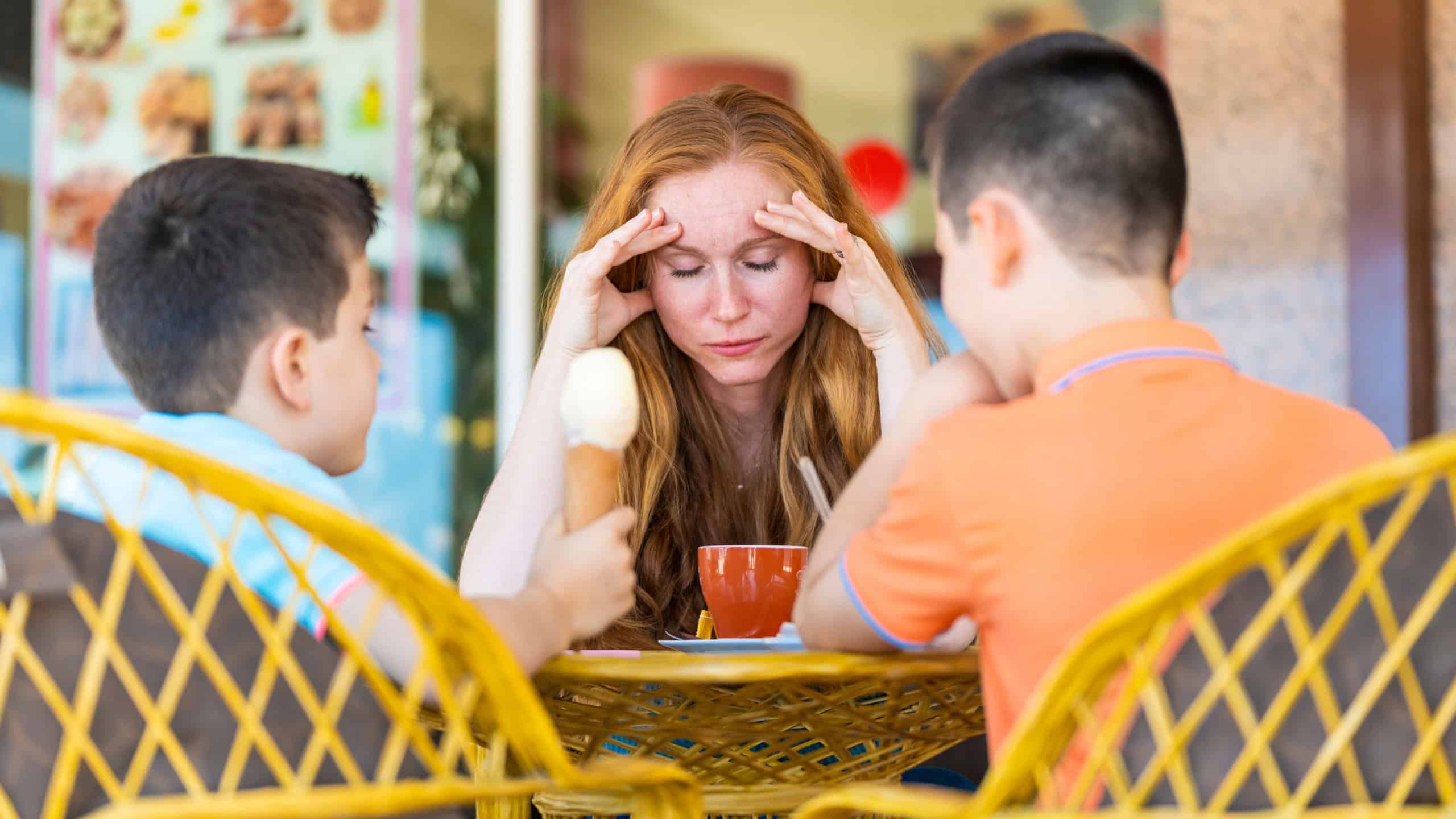 Stressed mother on a terrace of a coffee shop with her two children