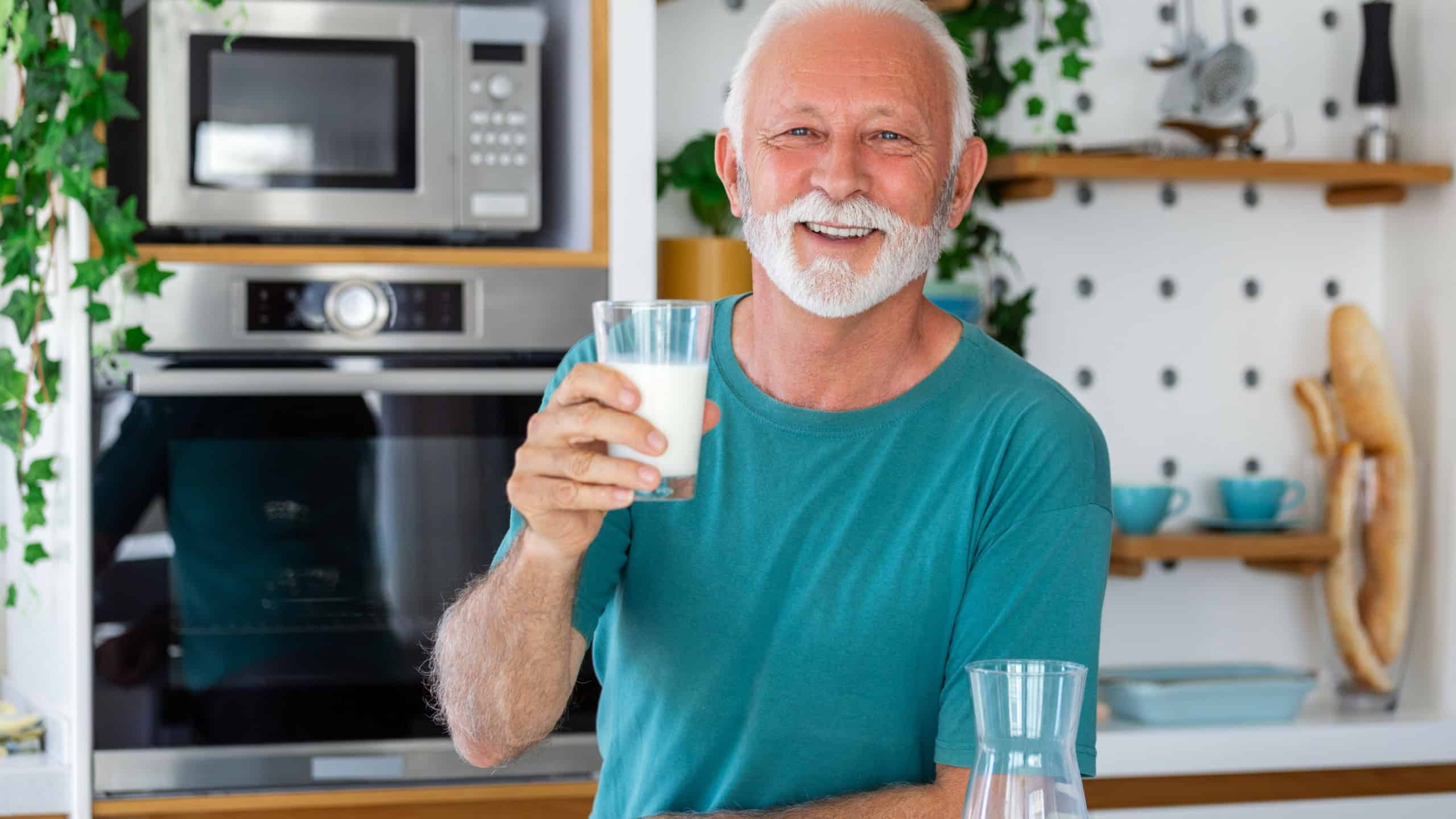 Senior man drinking a glass of milk with a happy face standing and smiling. Handsome senior man drinking a glass of fresh milk in the kitchen
